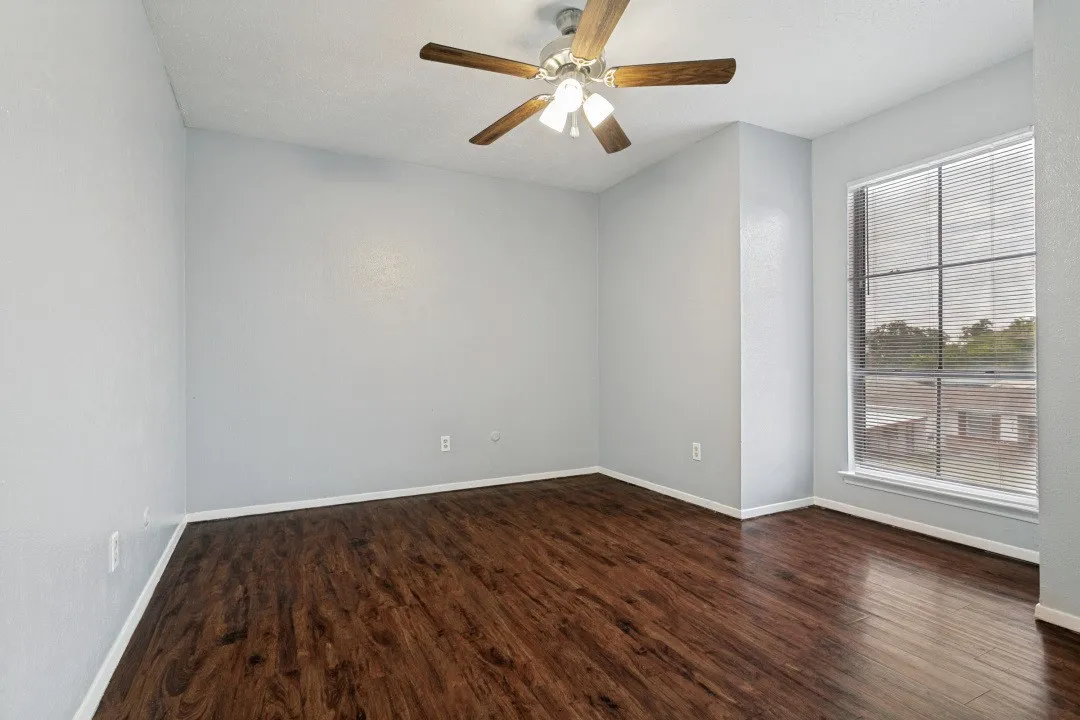 Wood-finish flooring, ceiling fan with integrated lighting, window with horizontal blinds, and neutral wall tones