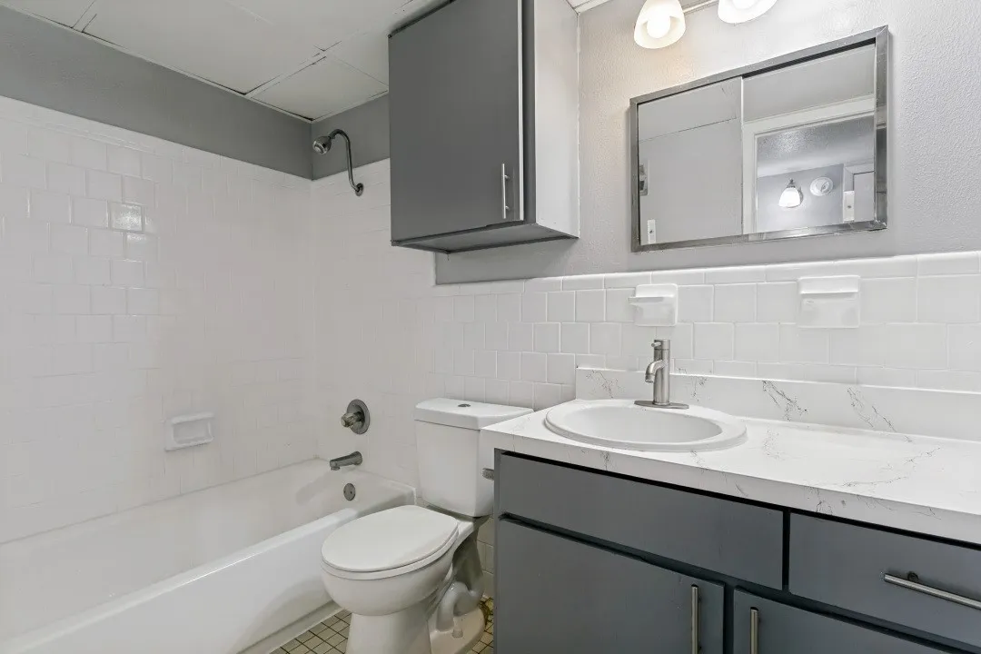 White subway tile shower surround with a built-in tub, a vanity with a white countertop and integrated sink, and gray cabinetry with brushed nickel hardware