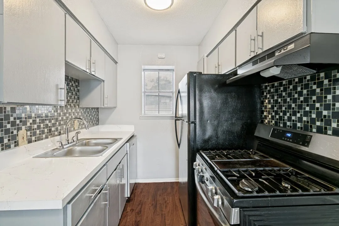 Kitchen featuring light-colored cabinetry, a dual-basin stainless steel sink, a mosaic tile backsplash, a black gas range, and wood-finish flooring