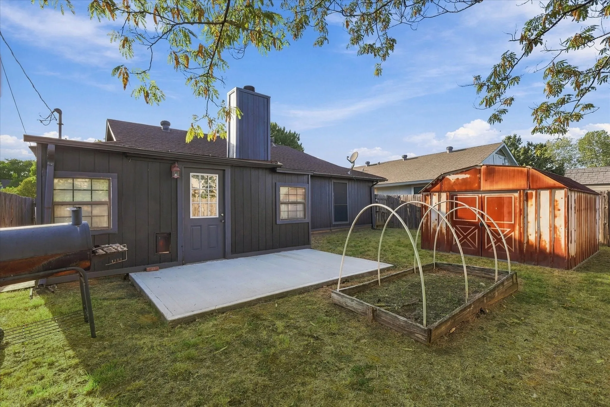 Rear exterior with concrete patio, board and batten siding, multiple windows, and detached storage structure