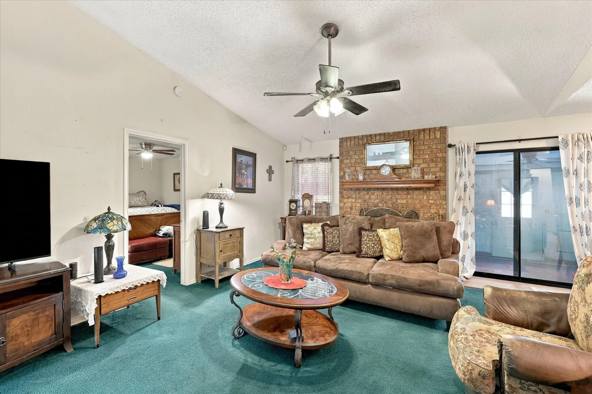 Vaulted ceilings, a brick-finish fireplace with a wood mantle, and sliding glass doors