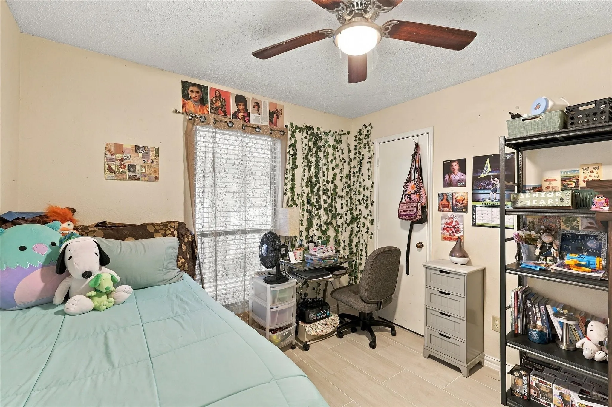 Neutral-toned walls with a textured ceiling, a window with horizontal blinds, and a ceiling fan with integrated lighting