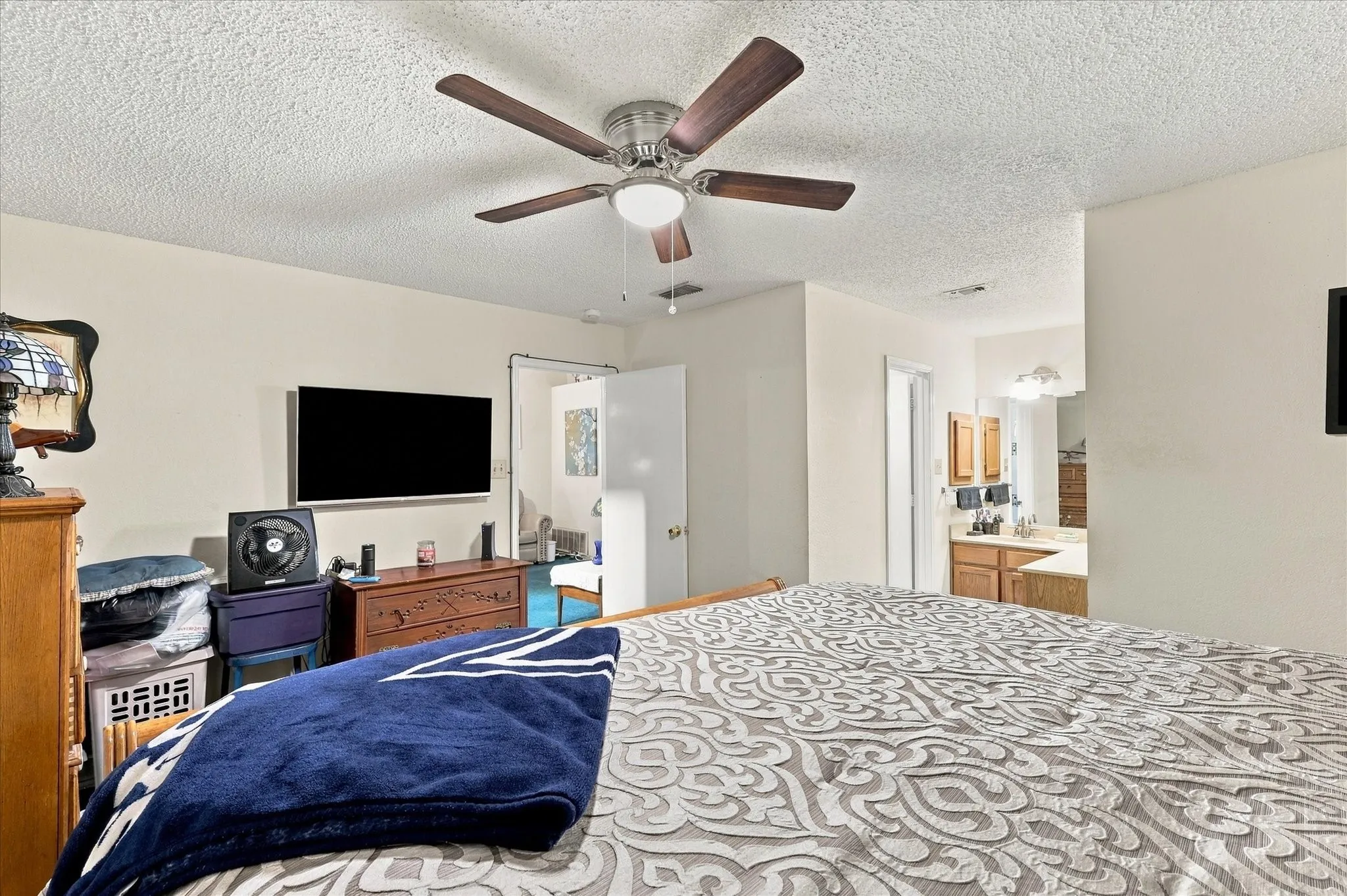 Recessed ceiling light with a ceiling fan, wall-mounted television, and a vanity with wooden cabinetry