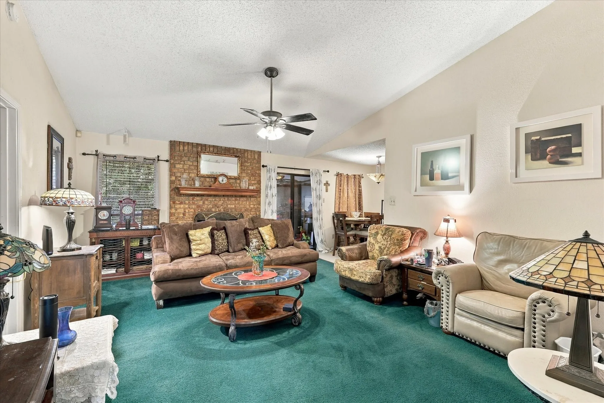 Vaulted ceiling featuring a ceiling fan, brick accent wall with a wood mantel, and green carpeting