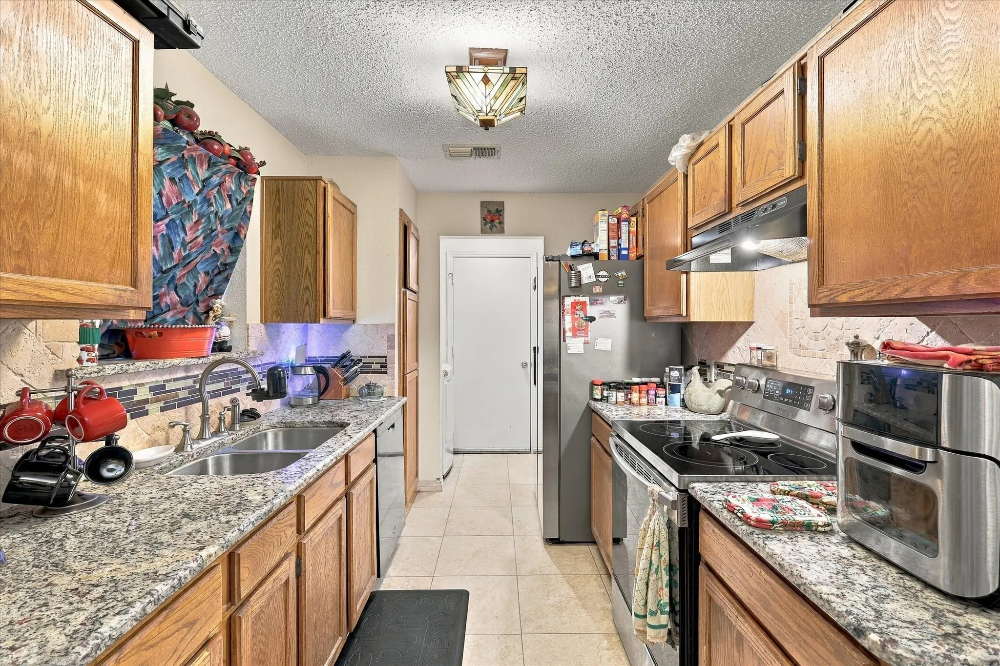 Galley kitchen featuring wood cabinetry, granite-style countertops, stainless steel appliances, and a tile backsplash