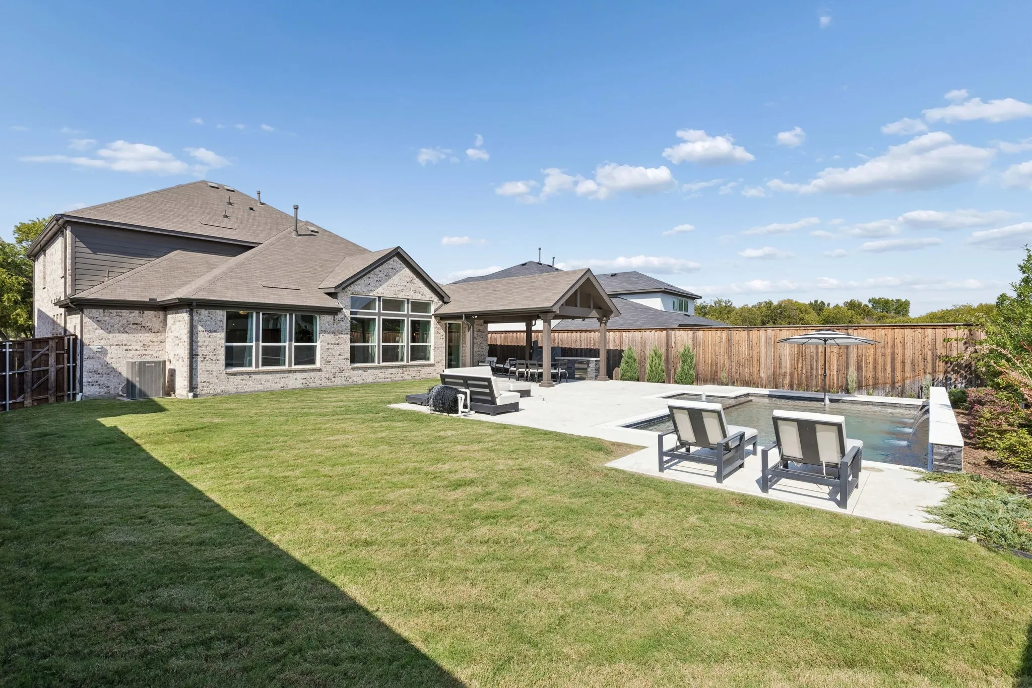 Beautifully landscaped backyard showcases the home’s spacious lawn, sparkling pool and spa, expansive patio areas, and covered outdoor living space, creating a private setting designed for effortless outdoor enjoyment.