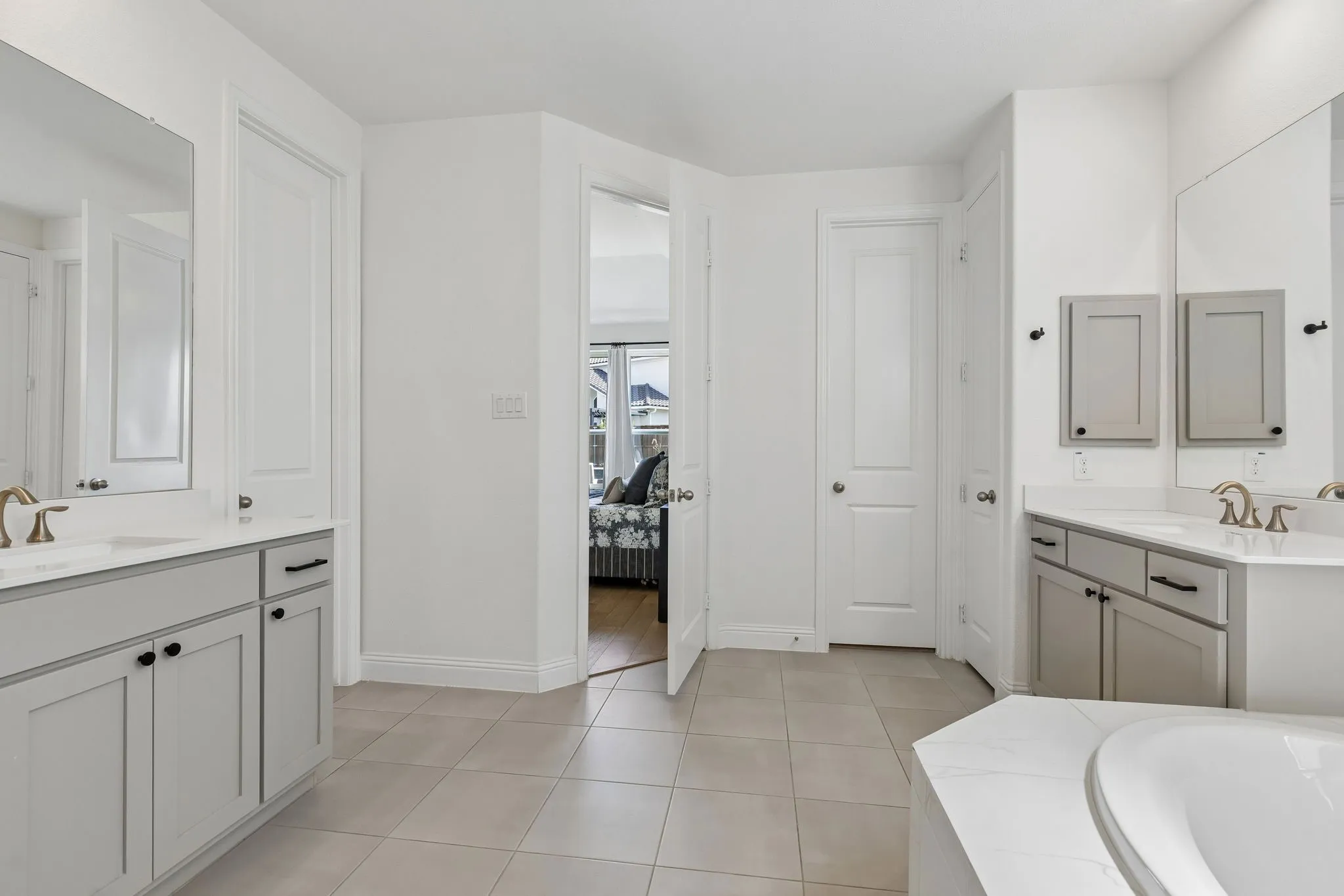 The spacious primary bath provides exceptional everyday functionality with dual vanities, ample cabinetry, oversized mirrors, water closet, linen closet, medicine cabinet, and a beautifully tiled bathing area. Generous floor space and abundant natural light contribute to the room’s open and tranquil feel.