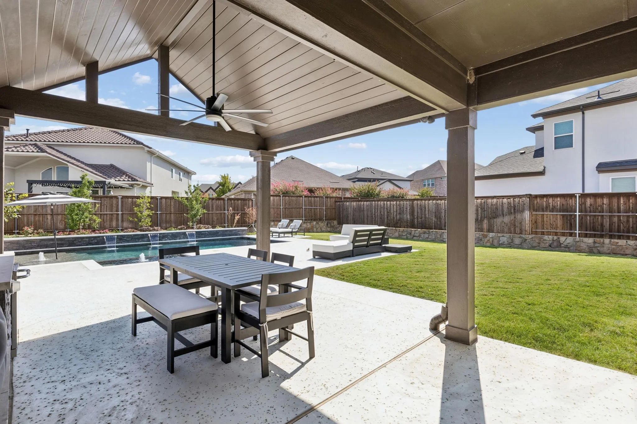 Generous covered patio creates an inviting outdoor living room with a vaulted ceiling, ceiling fan, dining area, and direct views of the pool and landscaped backyard—ideal for year-round entertaining.