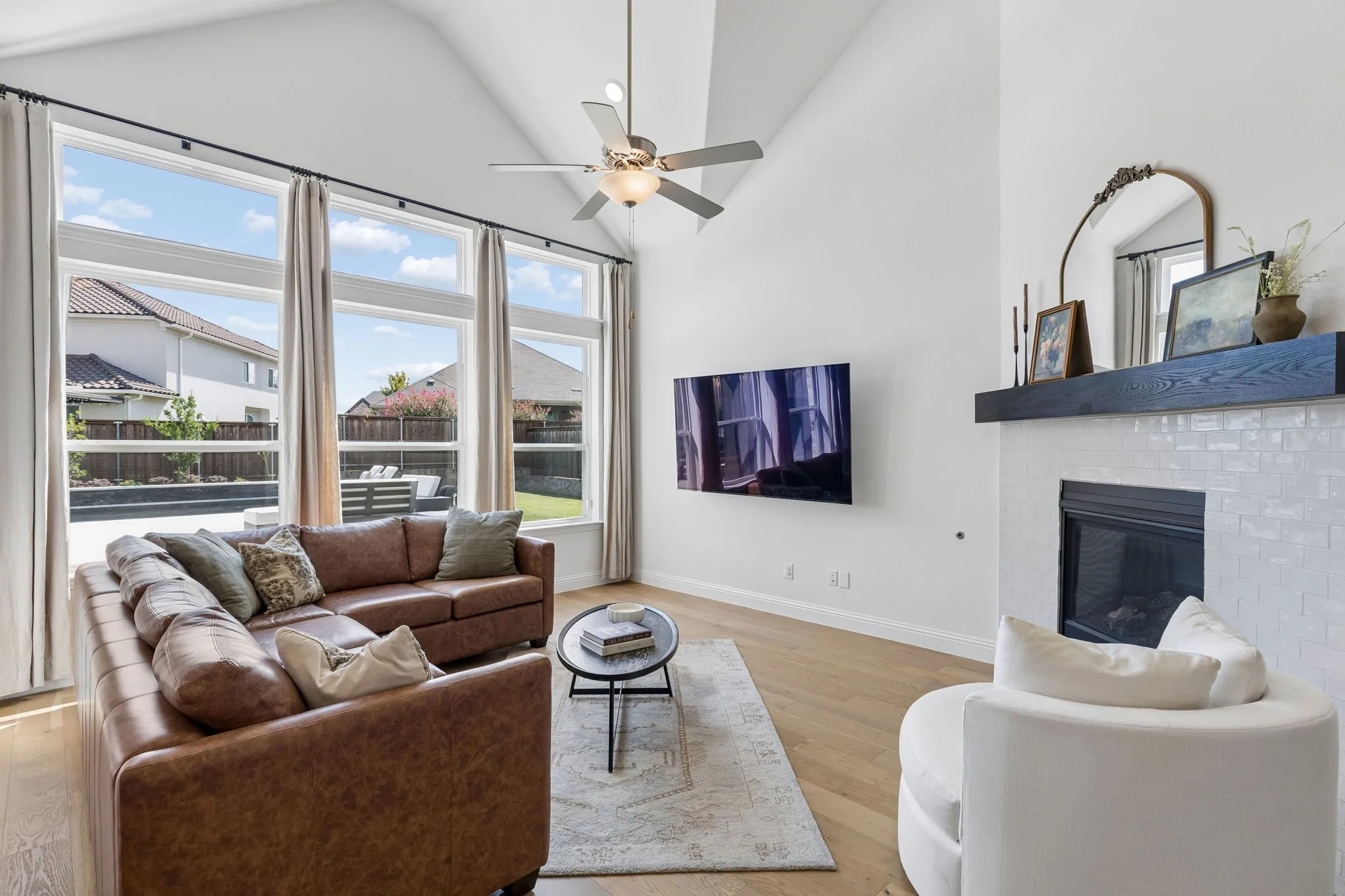 Light-filled and inviting, the living room features soaring ceilings, beautiful wood flooring, expansive windows, and a striking fireplace with a substantial wood mantel. The generous windows overlook the backyard, creating a wonderful connection between the comfortable interior and outdoor living spaces.