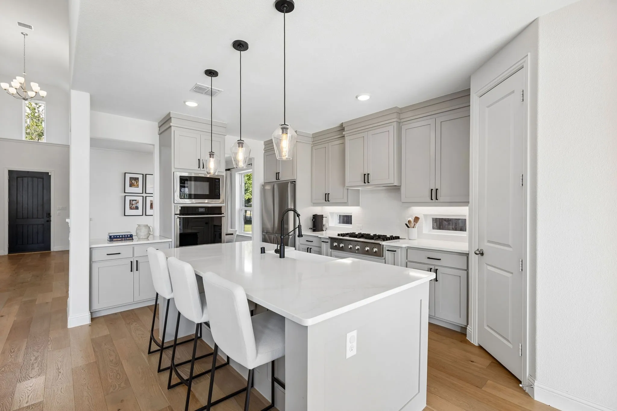 Open-concept kitchen showcases custom-style cabinetry, quartz countertops, stainless-steel appliances, a substantial center island, and warm wood flooring creating an effortless flow for entertaining.