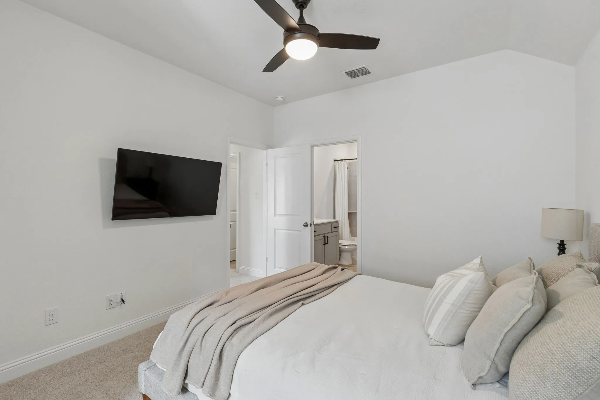 Another view of the spacious bedroom that offers a serene retreat with plush carpeting, ceiling fan, and direct access to the adjoining bathroom.