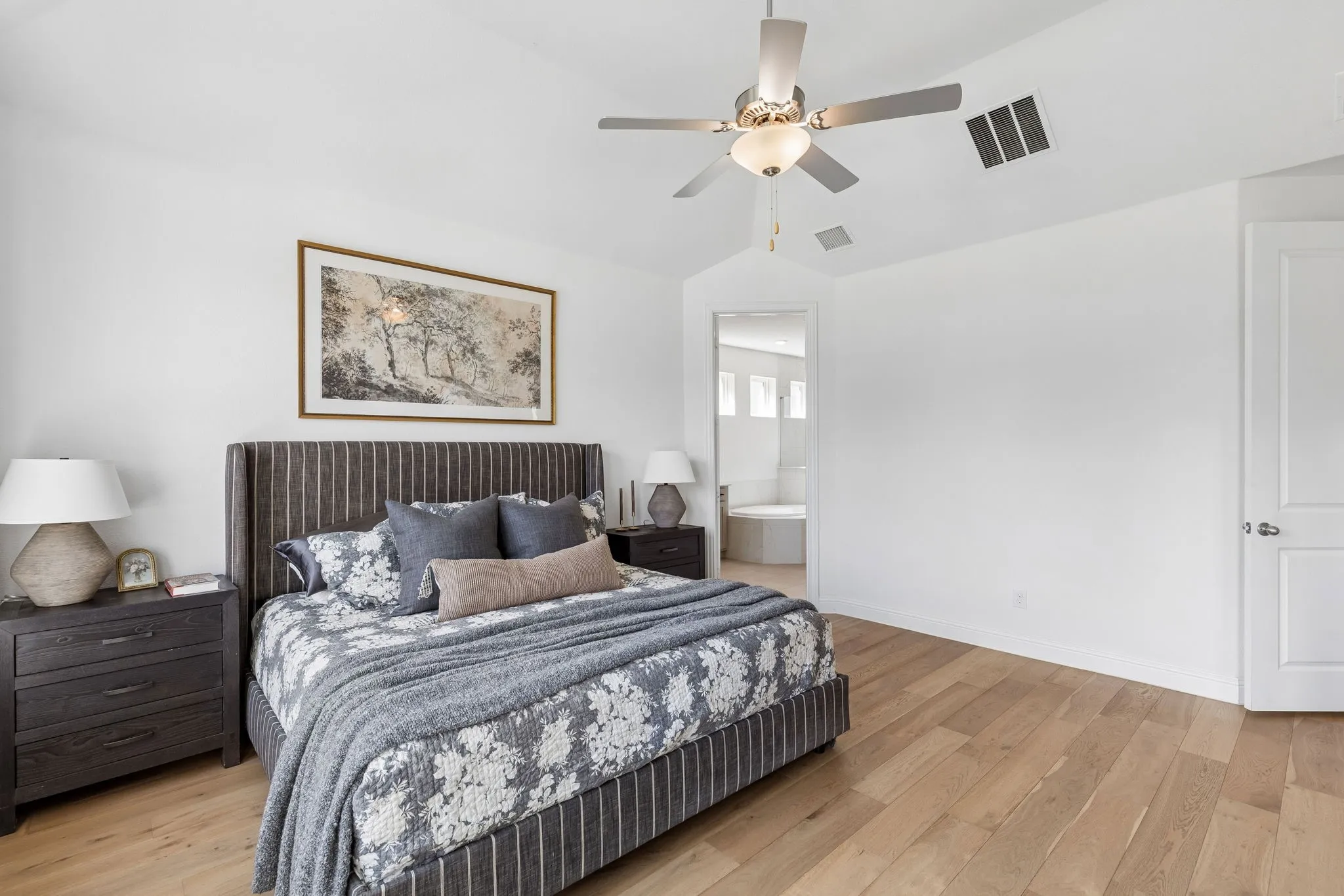 An additional view of the spacious primary retreat highlights its generous proportions, warm wood flooring, abundant natural light, and direct connection to the ensuite bath. The neutral palette creates a calm and timeless backdrop for everyday living.
