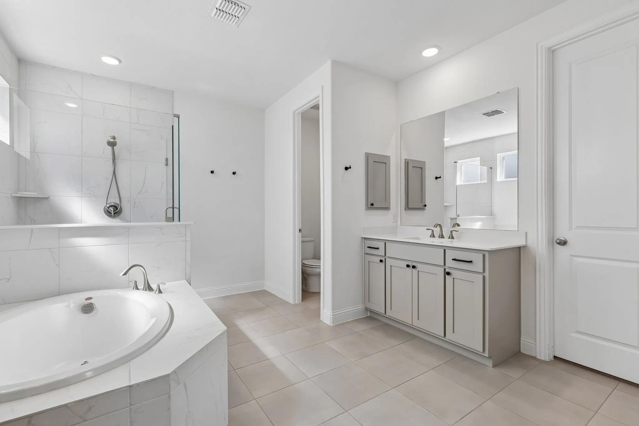 Thoughtfully designed for both function and relaxation, this expansive primary bath features dual vanities, extensive cabinetry, a deep soaking tub, and a glass-enclosed shower. The clean neutral palette and marble-inspired tilework lend an elegant, timeless feel.