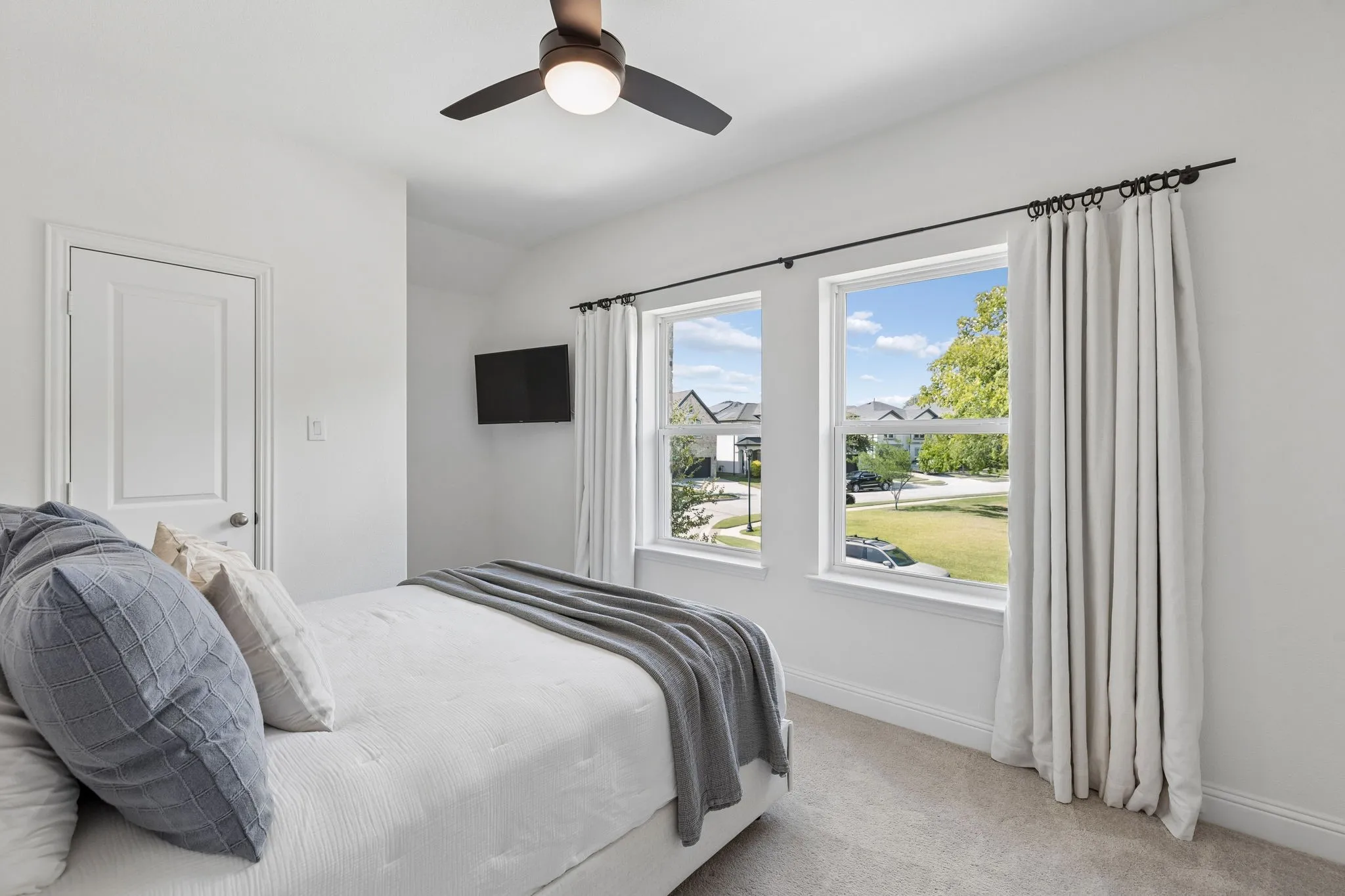 Light-filled secondary upstairs bedroom features a neutral palette, plush carpeting, and ceiling fan, creating a comfortable and inviting retreat.