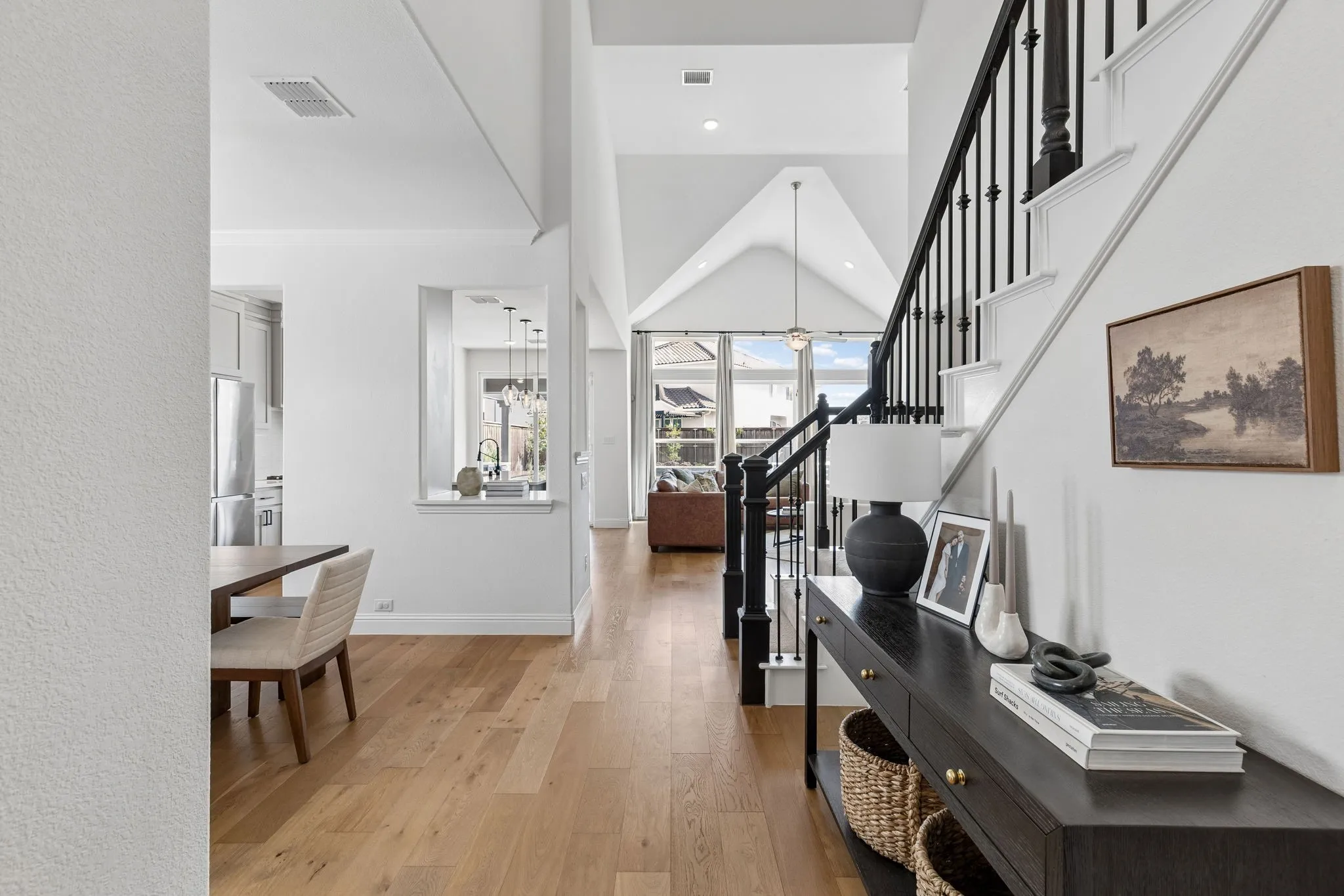 Welcoming entryway opens to a beautifully connected interior filled with natural light, warm wood flooring, and soaring architectural details. A striking staircase with elegant black iron balusters anchors the space, while sightlines extend toward the kitchen and living areas, highlighting the home's open and inviting design.