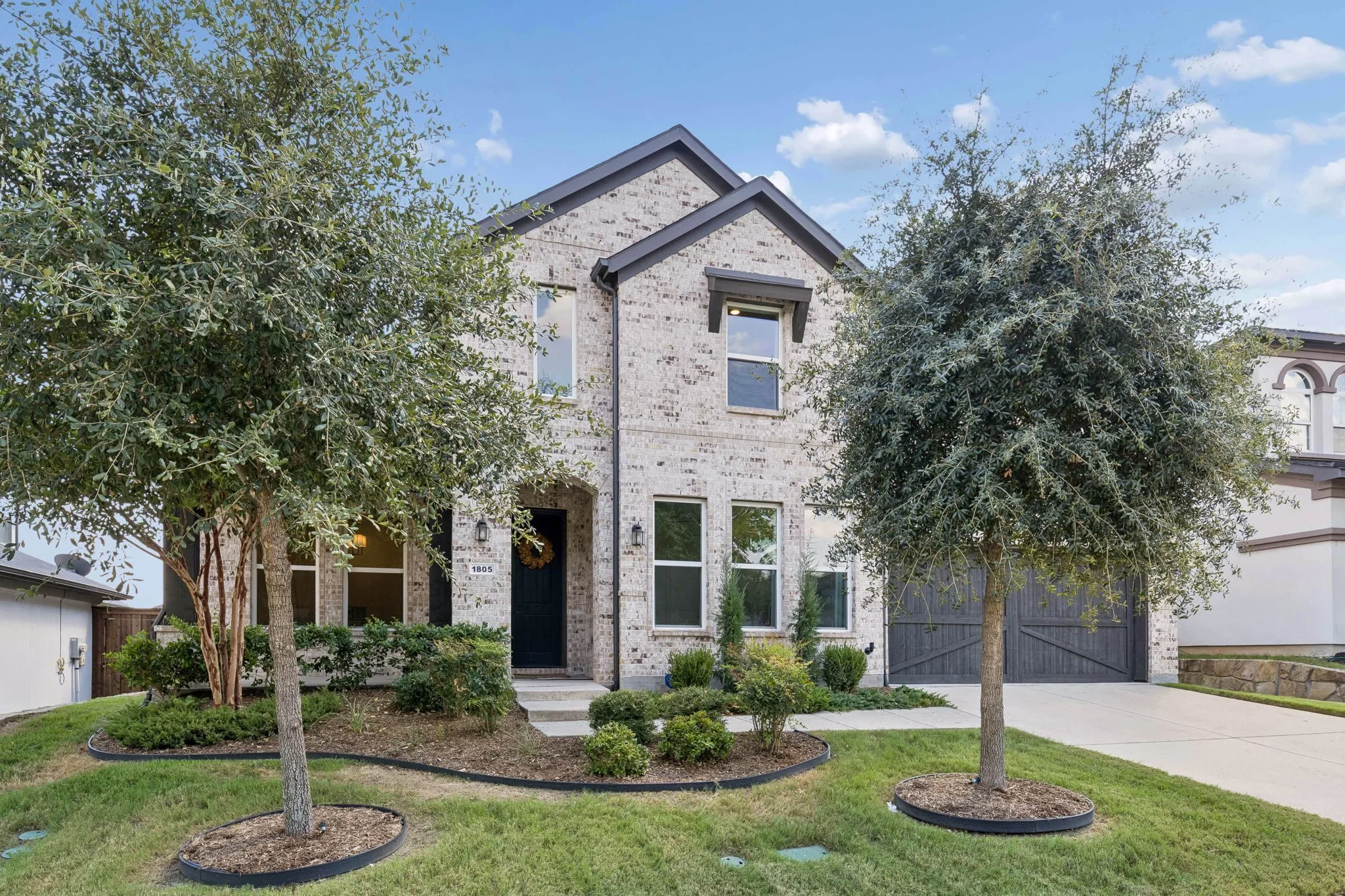 Beautiful curb appeal welcomes you to this thoughtfully designed two-story residence, framed by mature landscaping, manicured beds, and elegant light brick. A covered entry, striking dark front door, and handsome architectural detailing create a warm and inviting first impression.
