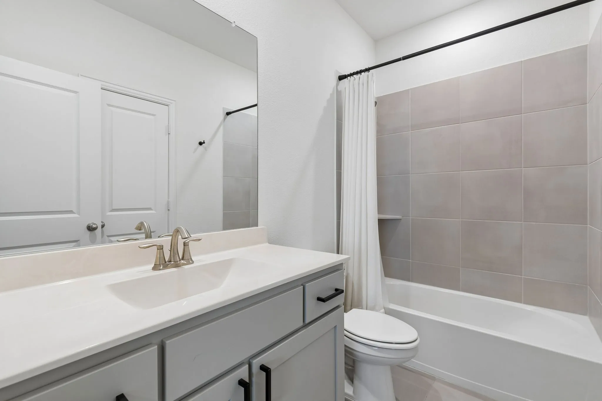 Clean, contemporary ensuite bathroom features a generous vanity, abundant counter space, oversized mirror, updated fixtures, and a neutral tile-surround tub.