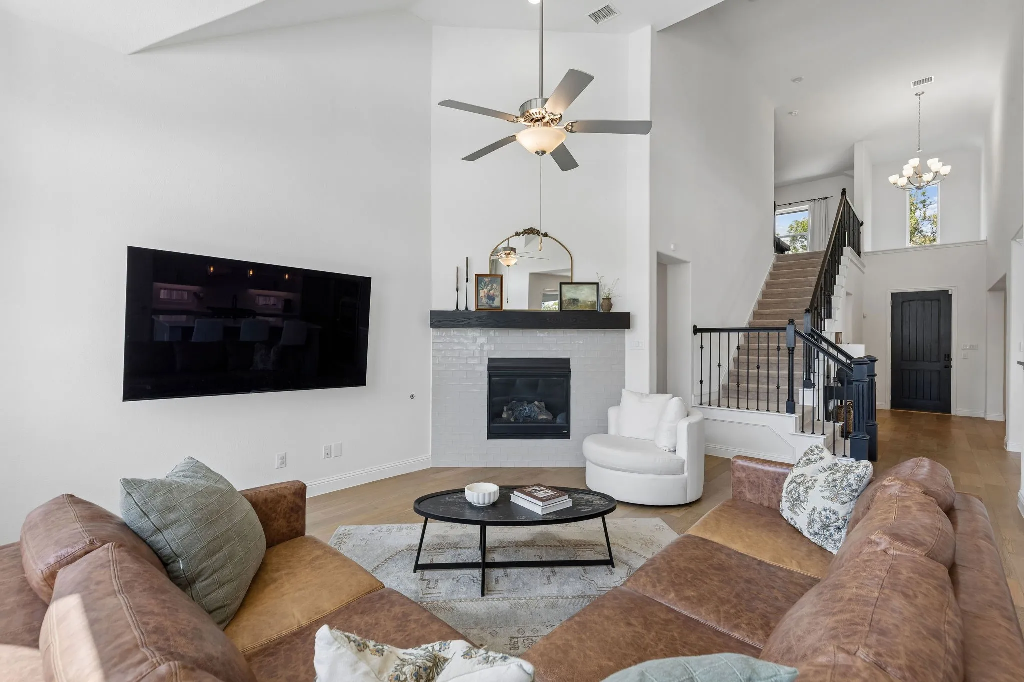 Designed for both relaxed evenings and effortless entertaining, this spacious living area centers around a beautifully finished fireplace and generous gathering space. Soaring ceilings, warm wood floors, abundant natural light, and the open staircase create an airy and sophisticated atmosphere.