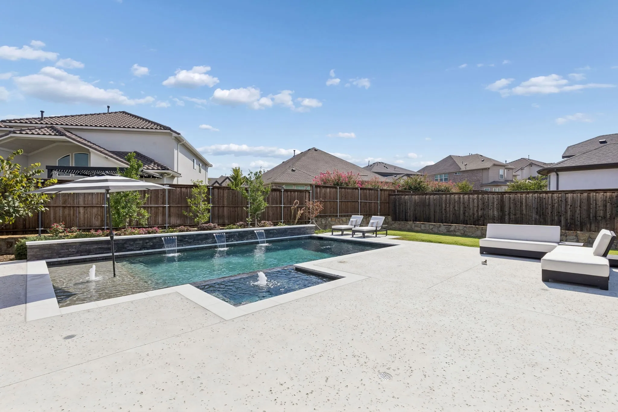 Private backyard oasis showcases a beautifully designed pool and spa surrounded by expansive entertaining areas, lush landscaping, and a full privacy fence. Multiple water features add a tranquil touch, while the generous pool deck provides plenty of room for lounging, entertaining, and soaking up the Texas sunshine.