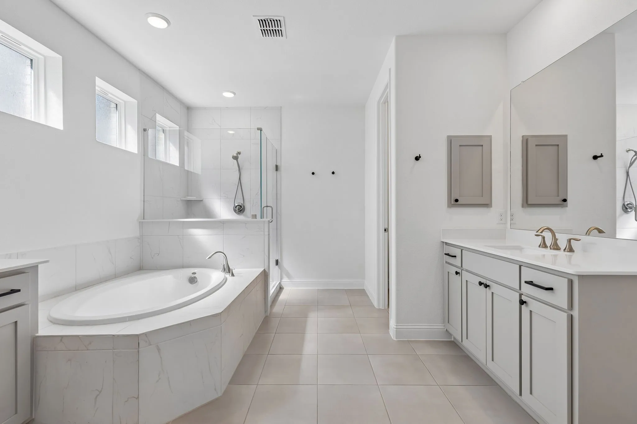 A spacious primary bath combines comfort and functionality with dual vanities, generous storage, a large soaking tub, and a beautifully tiled walk-in shower. Soft neutral finishes and abundant natural light create a fresh, serene setting for the start and end of each day.