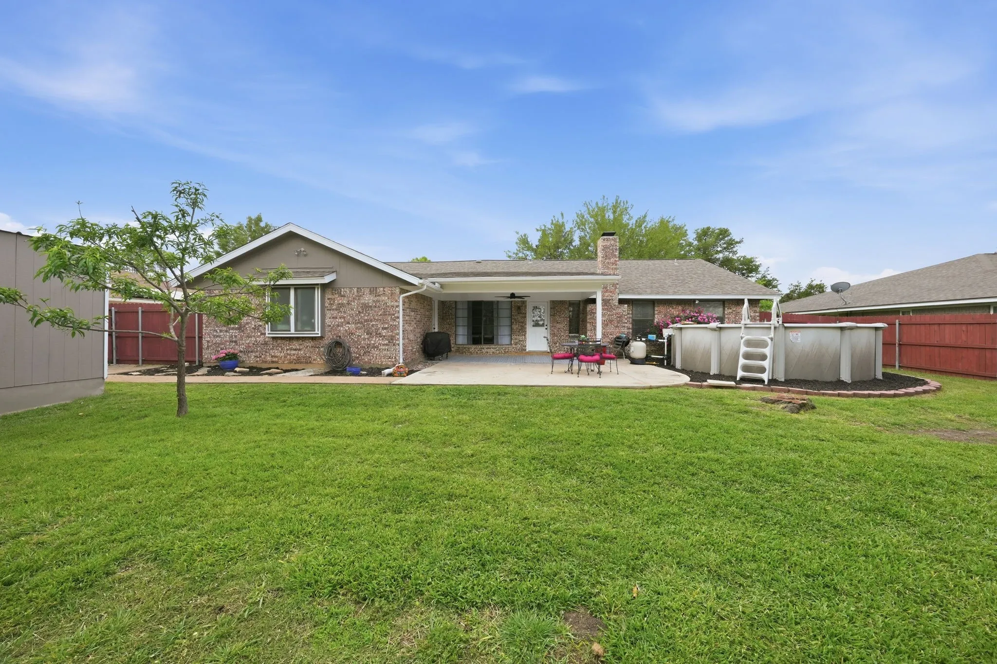 Expansive green lawn with a detached storage shed, brick exterior, covered patio, and an above-ground pool