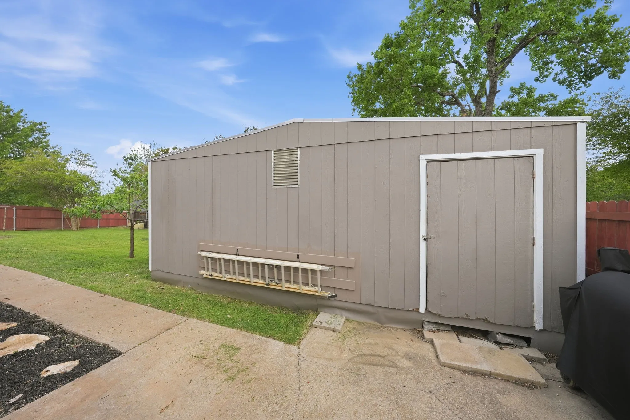 Outdoor storage structure with a paneled exterior, a single entry door, and a louvered vent