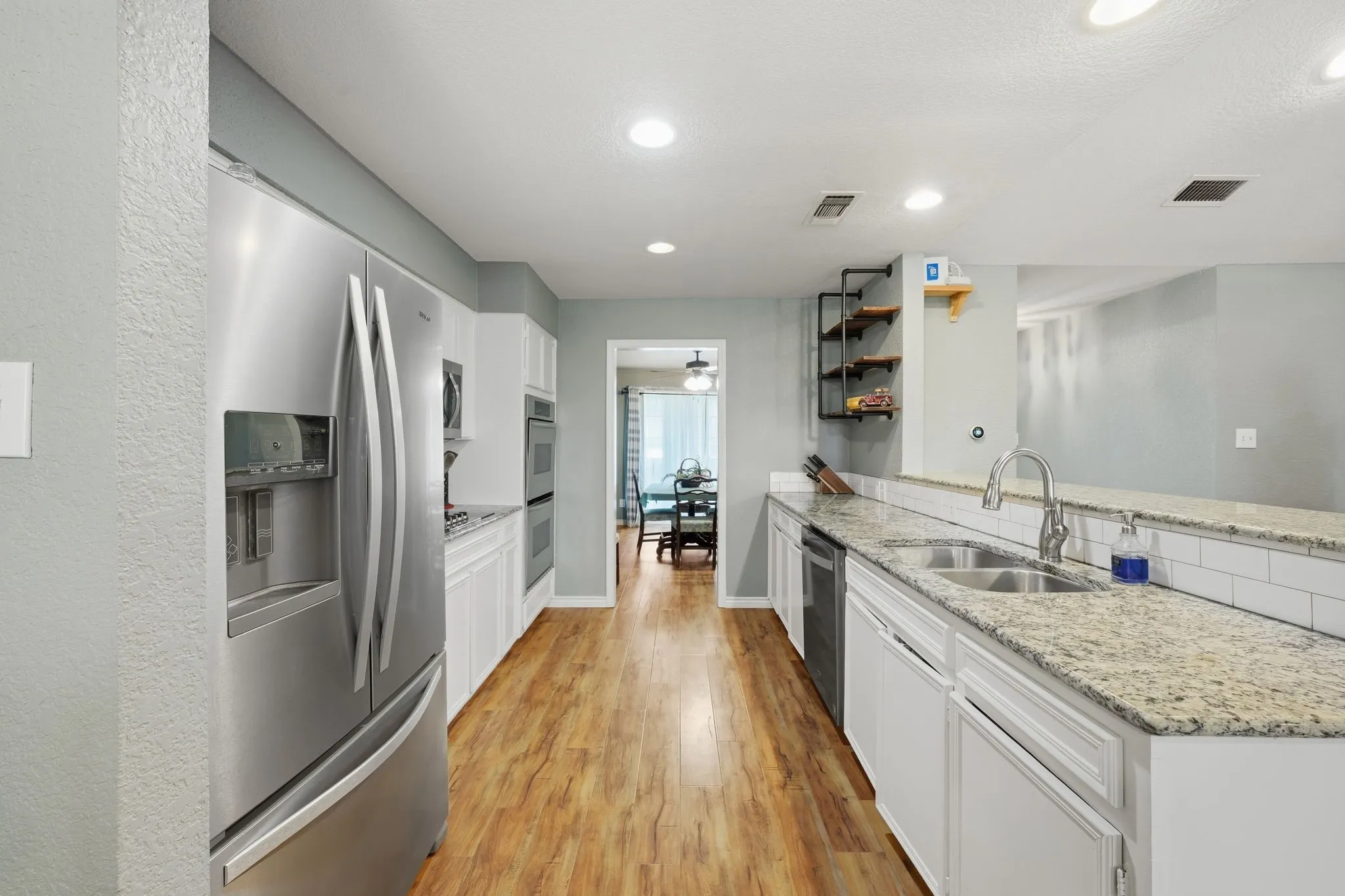 Kitchen featuring wood-finish flooring, white cabinetry, granite countertops, and stainless steel appliances