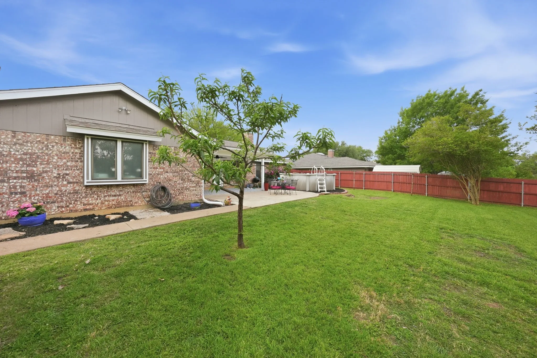 Expansive backyard featuring a manicured lawn, a paved patio, and a red wood fence