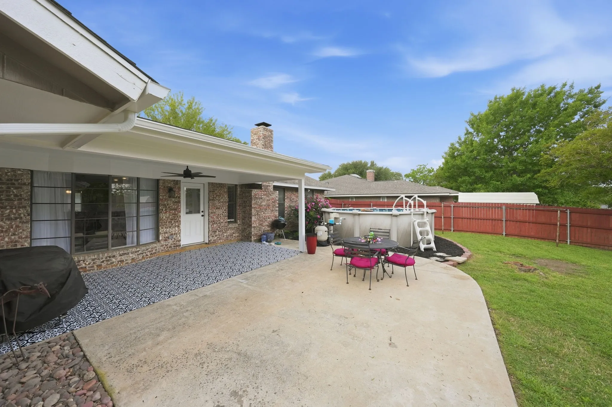 Rear exterior with a covered patio, brick facade, above-ground pool, and a fenced yard