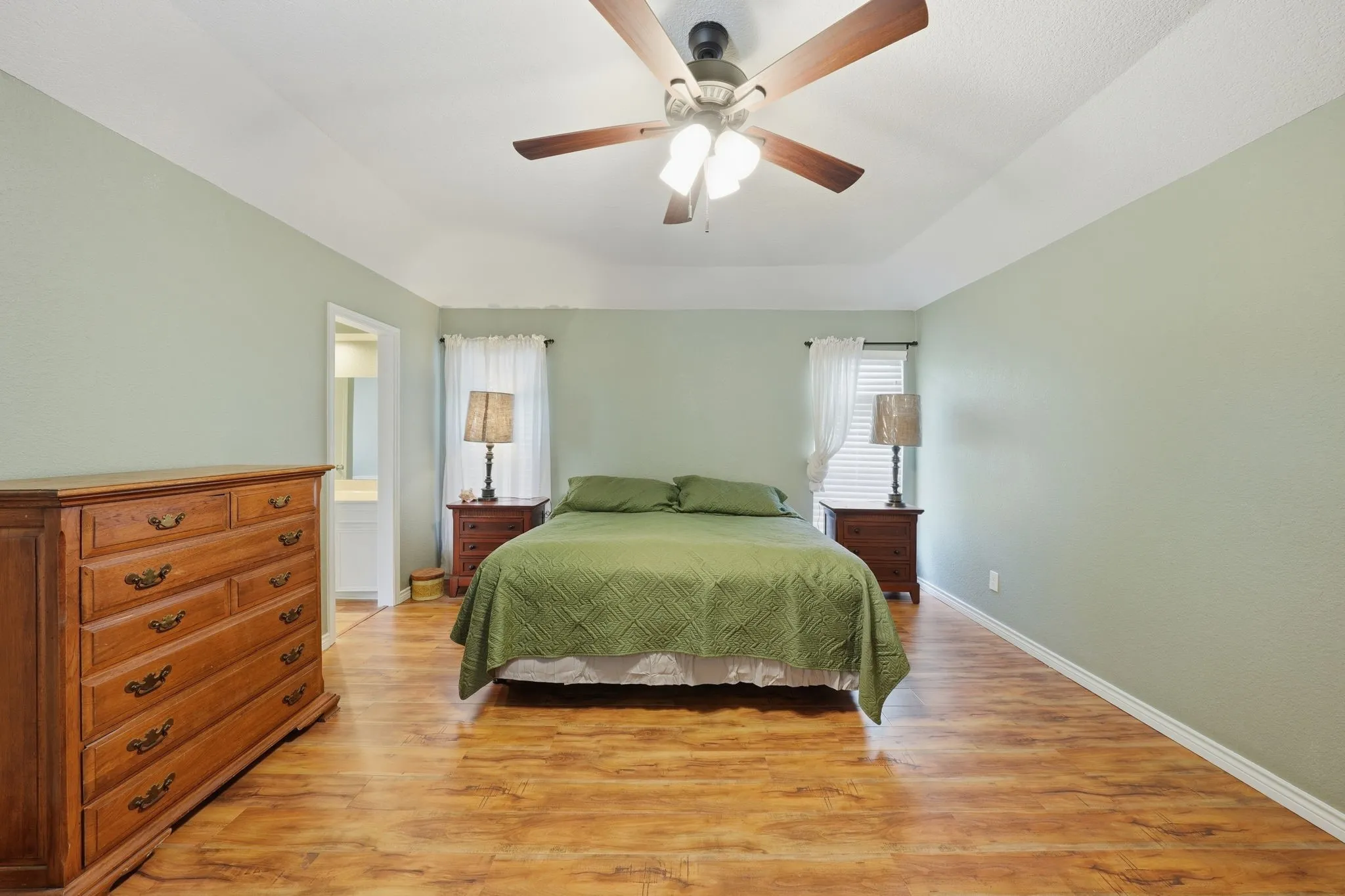 Primary bedroom with tray ceiling with a ceiling fan, wood-finish flooring, and light green walls