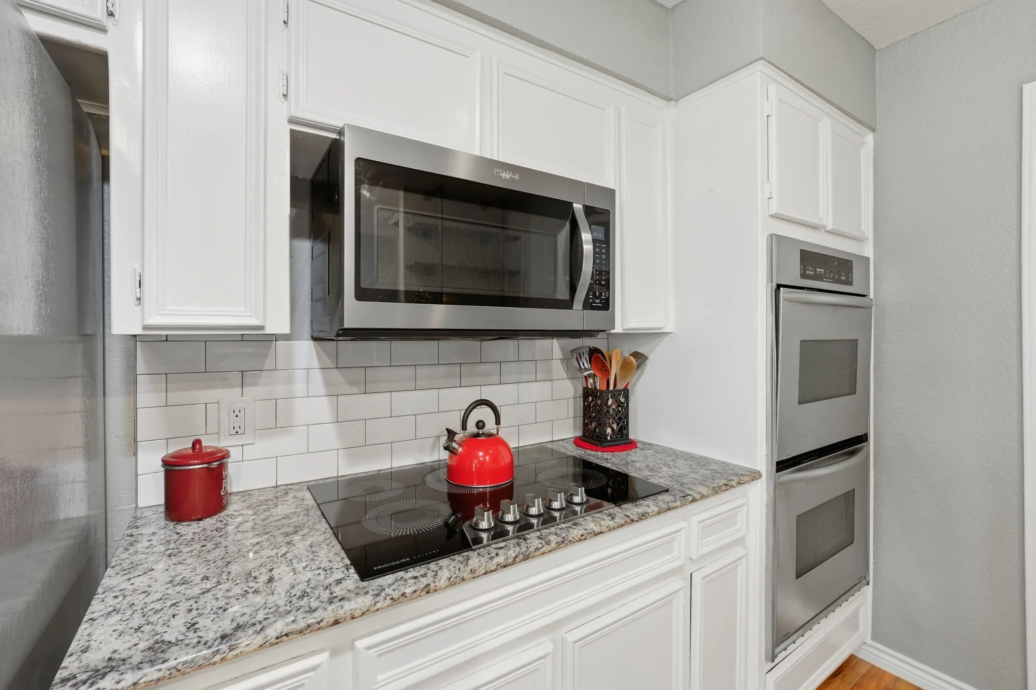 White cabinetry, built-in double ovens, stainless steel microwave, cooktop, and light-toned countertops