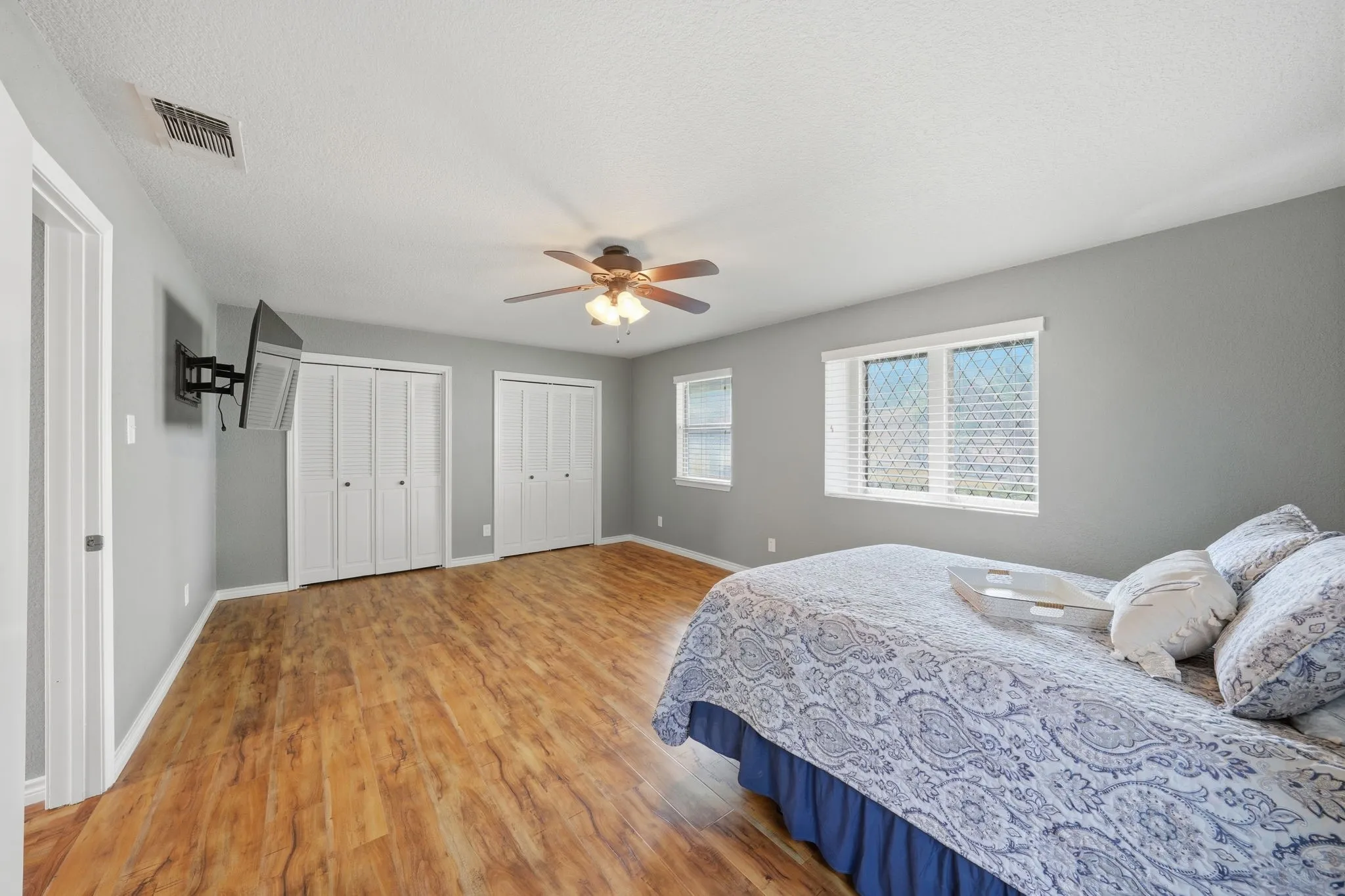 Wood-finish flooring, multiple windows, ceiling fan, and white bi-fold closet doors
