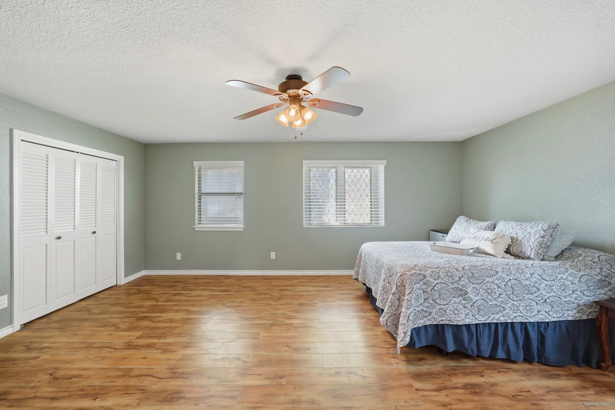Wood-finish flooring, two windows with blinds, bi-fold closet doors, and ceiling fan with light kit