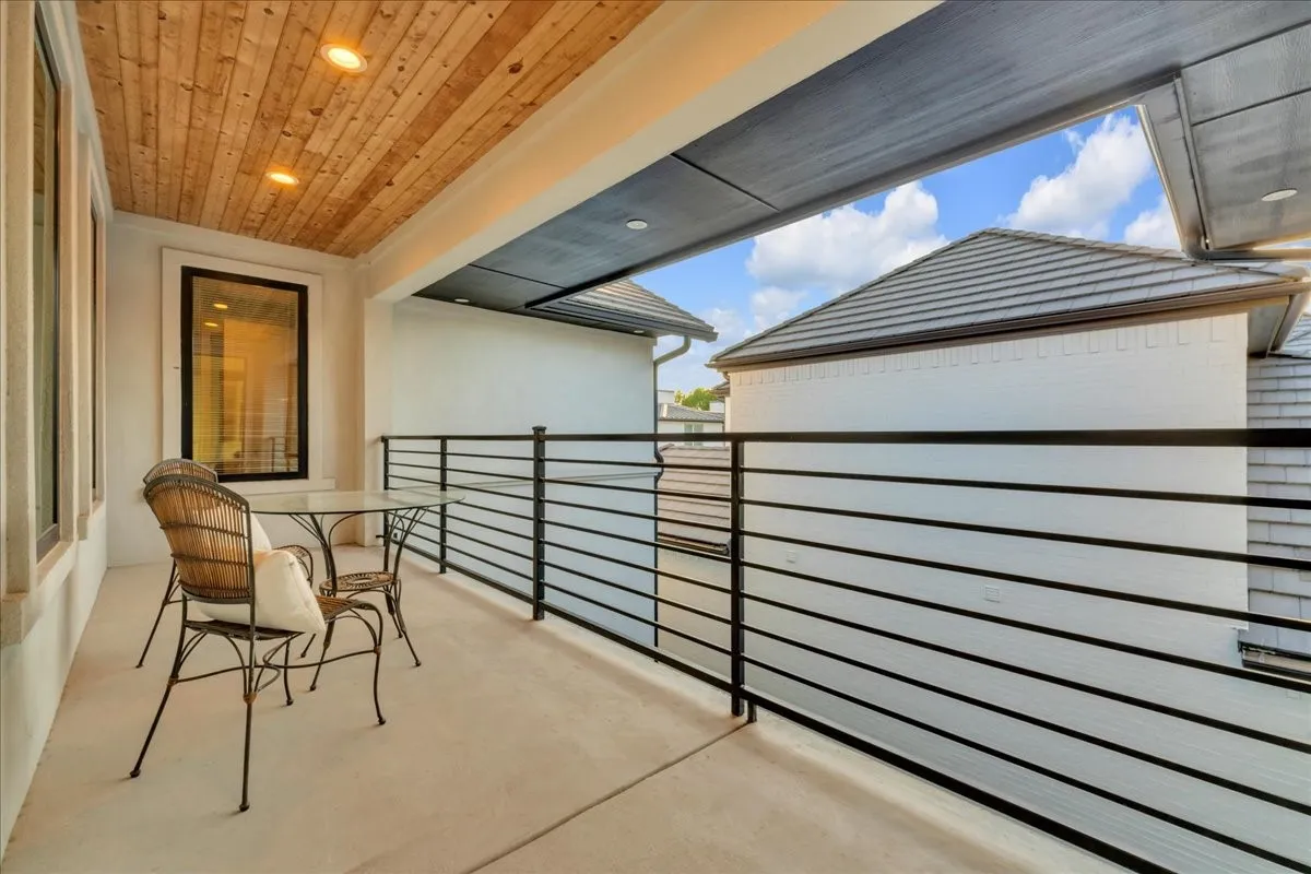 Covered outdoor balcony featuring a wood-panel ceiling with recessed lighting, a concrete floor, and black horizontal railings