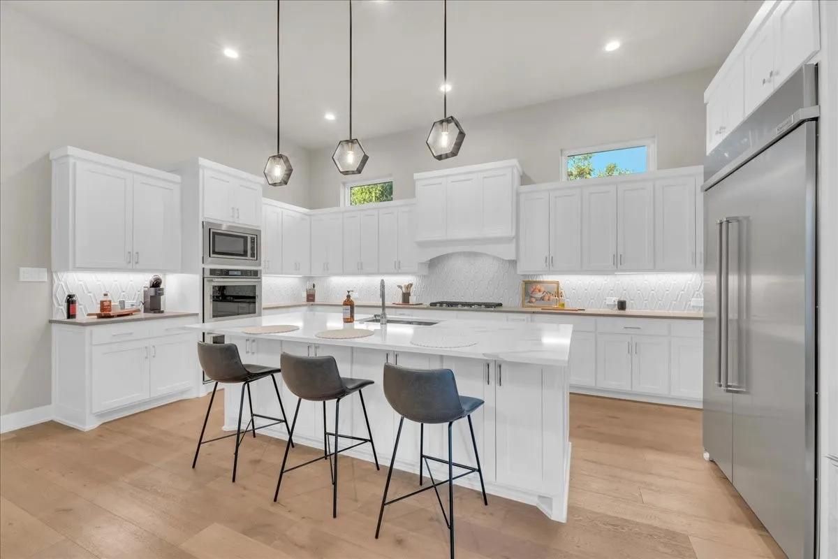 Gourmet kitchen featuring a large central Quartz island, white soft closed cabinetry, stainless steel appliances, and wood flooring