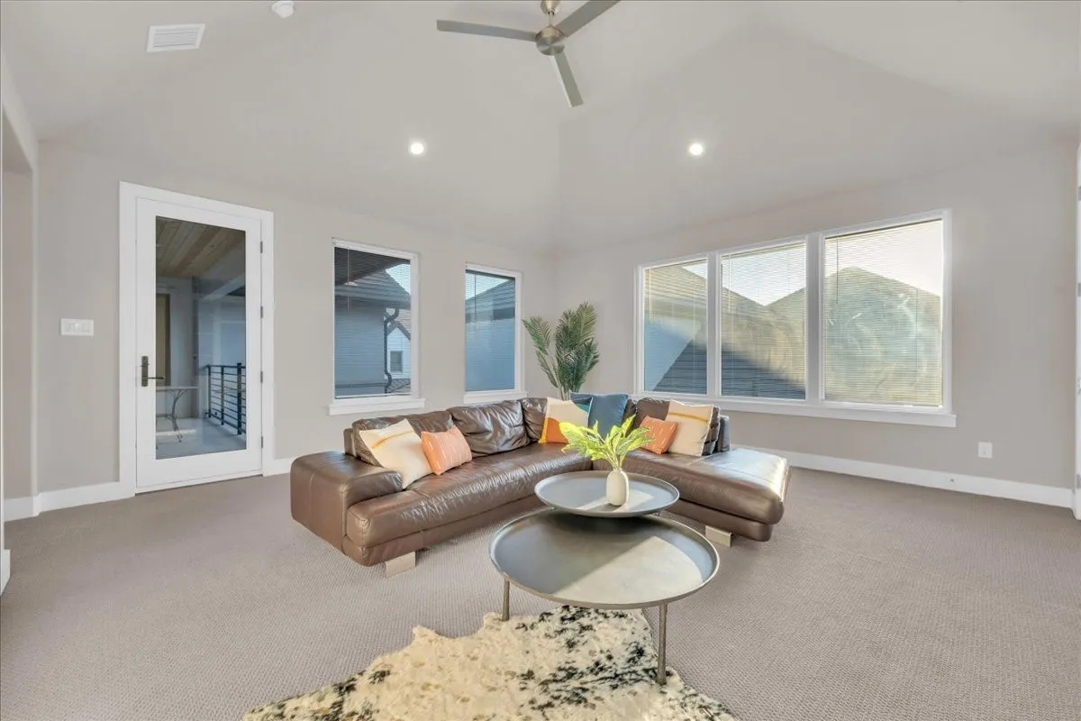 Vaulted ceiling with recessed lighting and ceiling fan, multiple large windows, and a glass-paneled door leading to an outdoor space