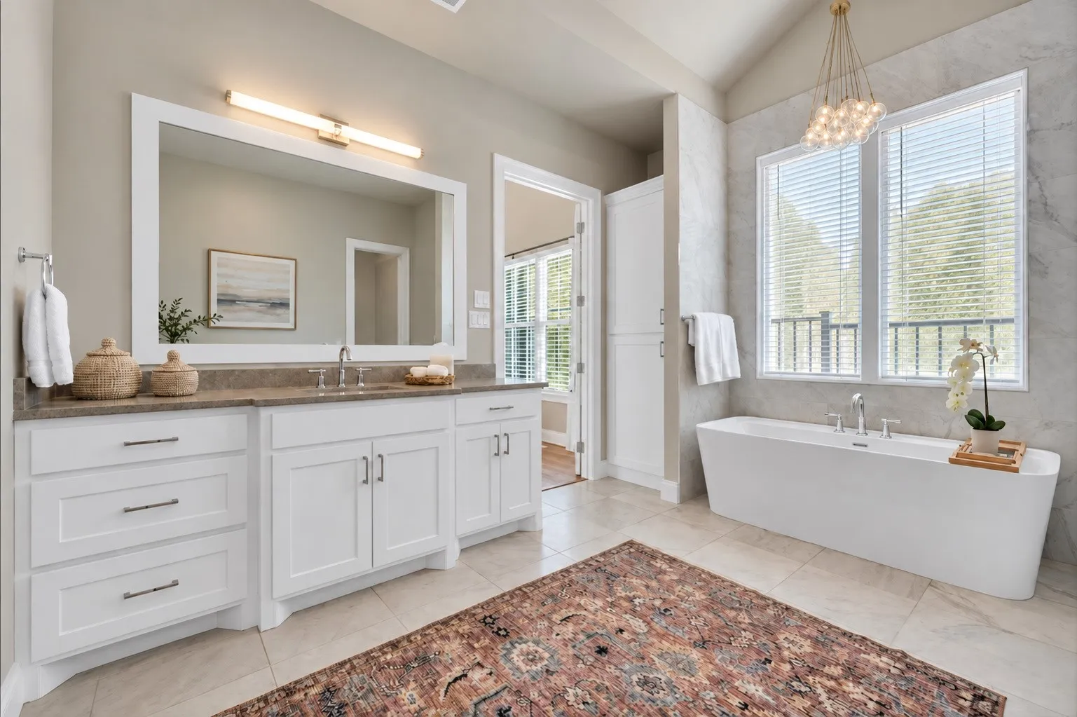 Dual sink vanity with white cabinetry and stone countertop, and an integrated rectangular mirror with a freestanding bathtub.