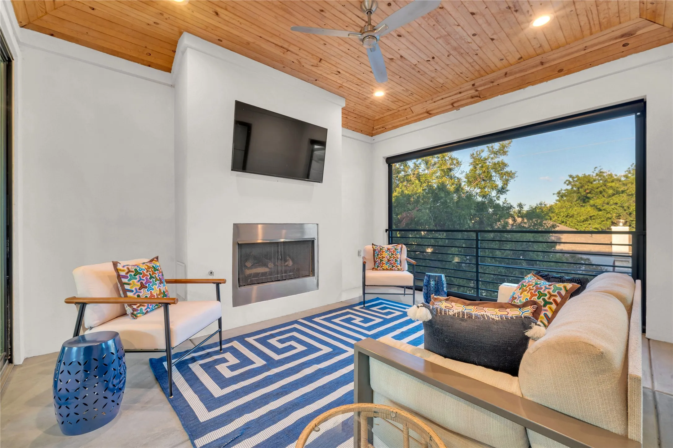 Upstairs outdoor living.  Wood-paneled ceiling, recessed lighting, ceiling fan, built-in fireplace with a stainless steel face, and a balcony with metal railings