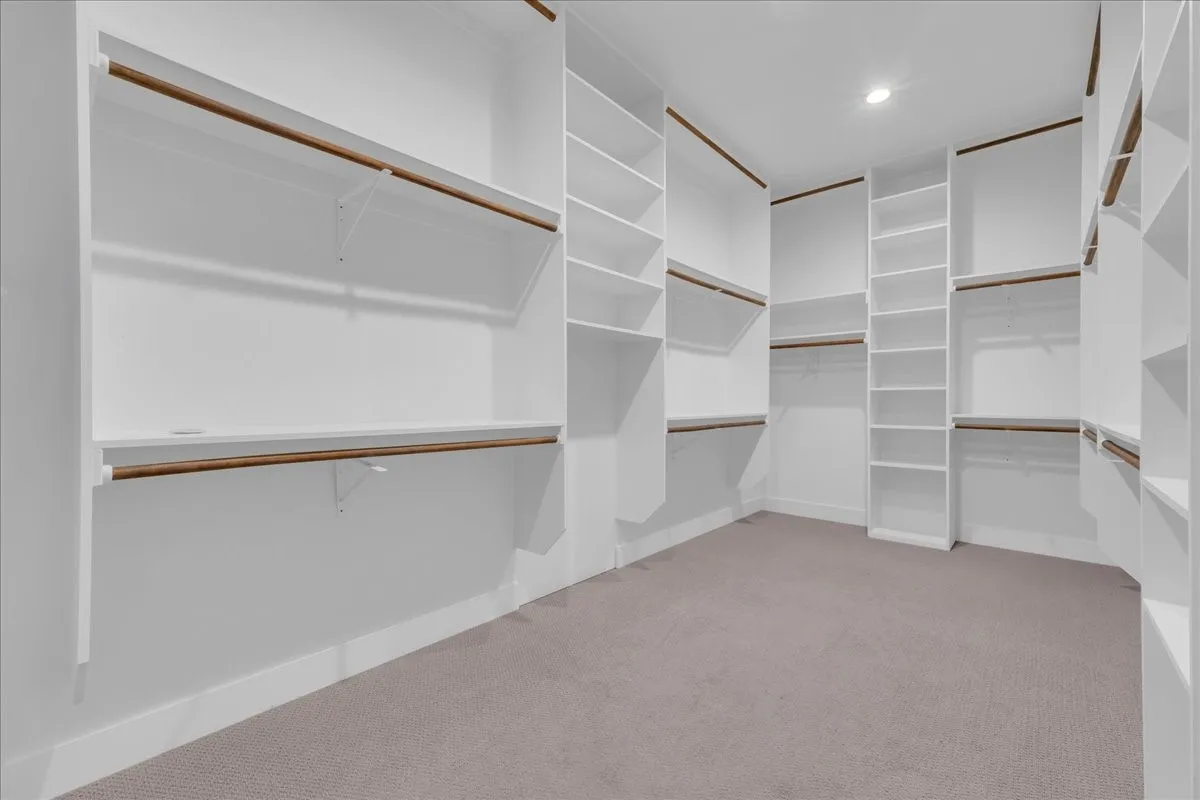 Spacious walk-in closet featuring white built-in shelving, multiple hanging rods, and recessed lighting