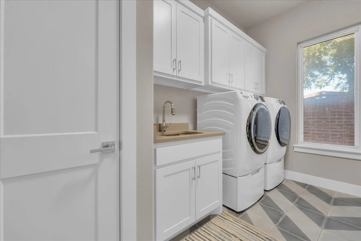 White cabinetry, light-toned countertop with an undermount sink, geometric pattern floor tile, and a window providing natural illumination