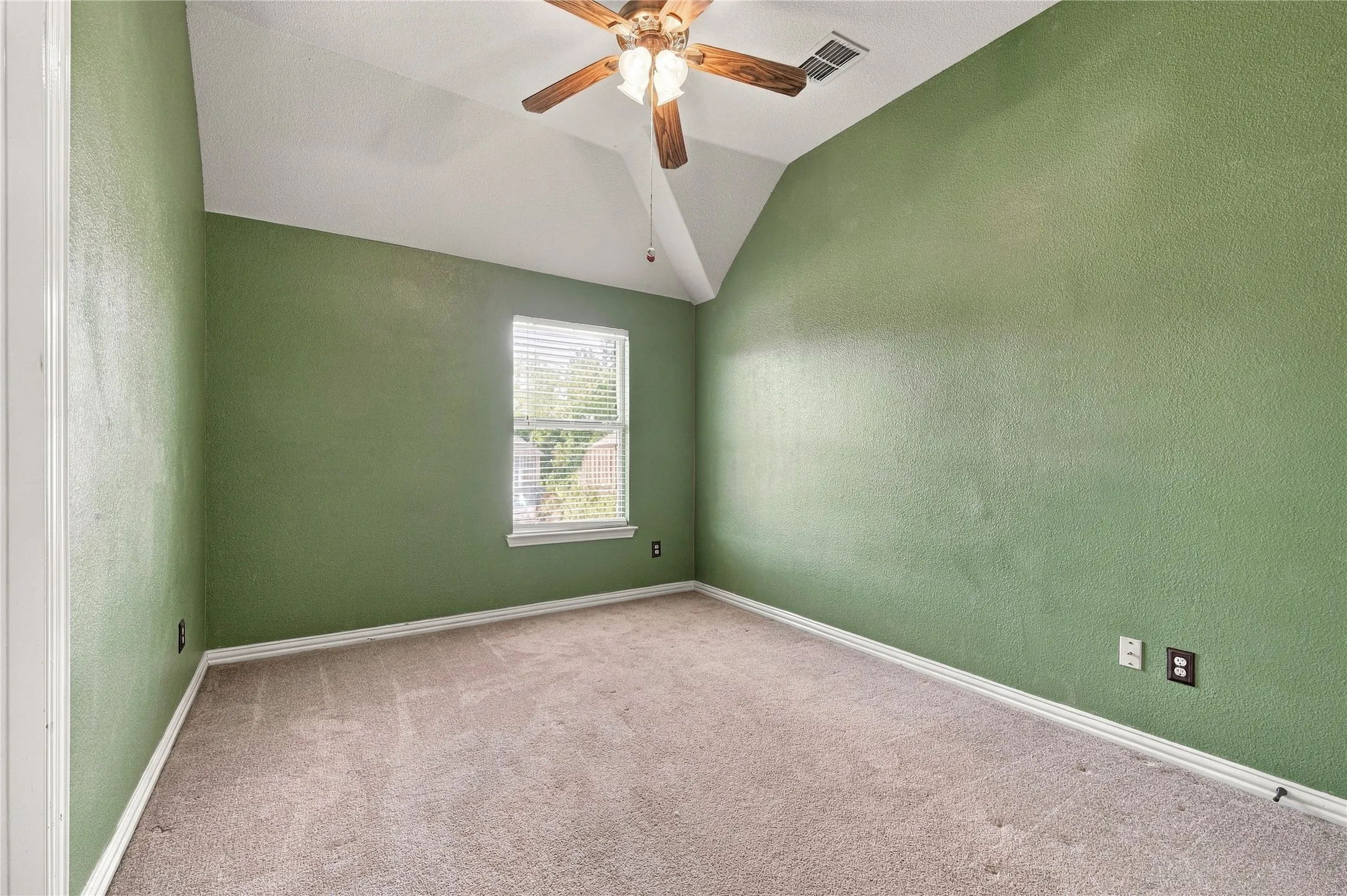 Vaulted ceiling, ceiling fan with integrated lighting, single window with blinds, carpet flooring, and painted walls