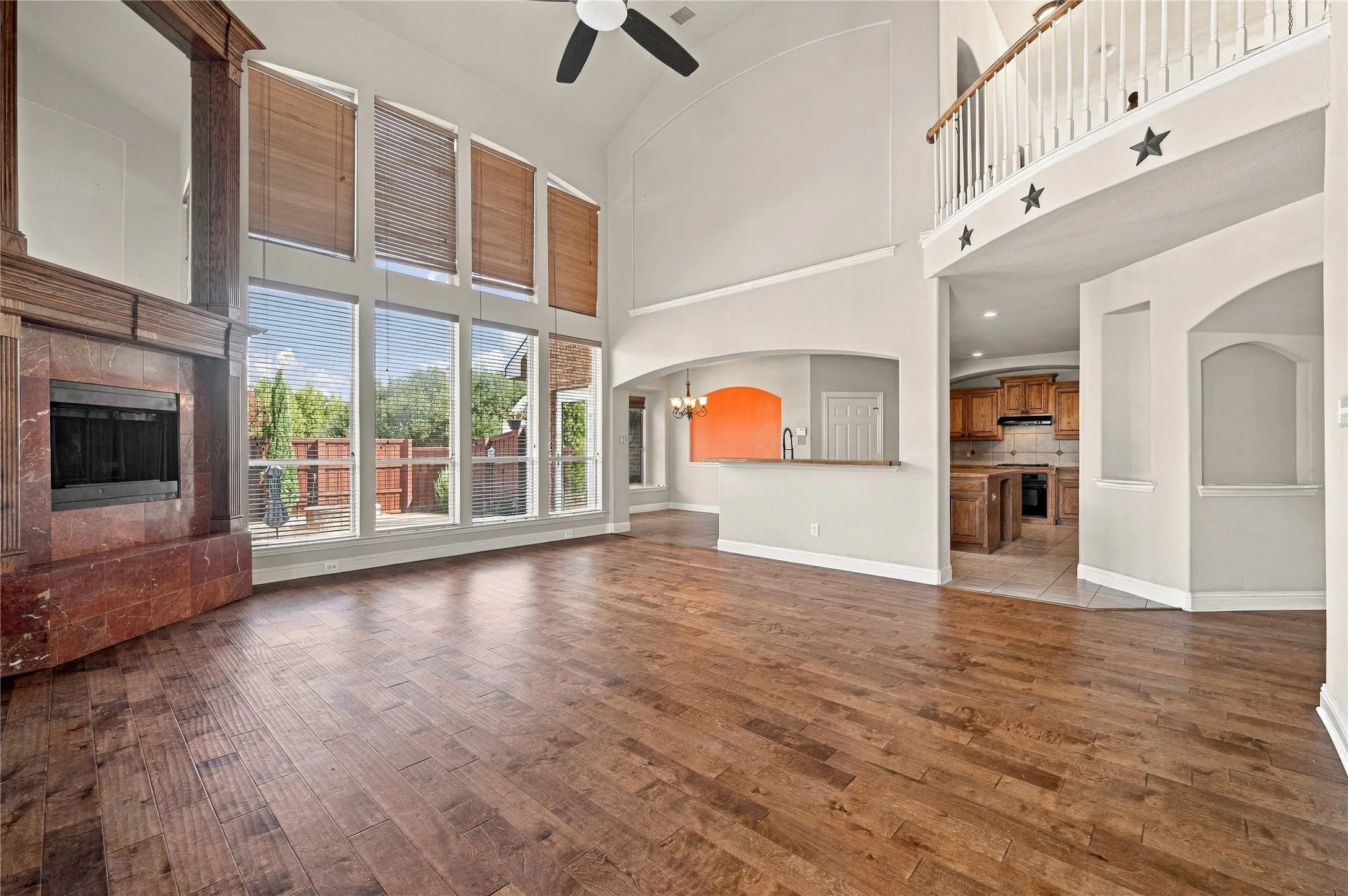 Vaulted ceilings with a ceiling fan, a large fireplace with a wood mantel, wood-finish flooring, and expansive windows