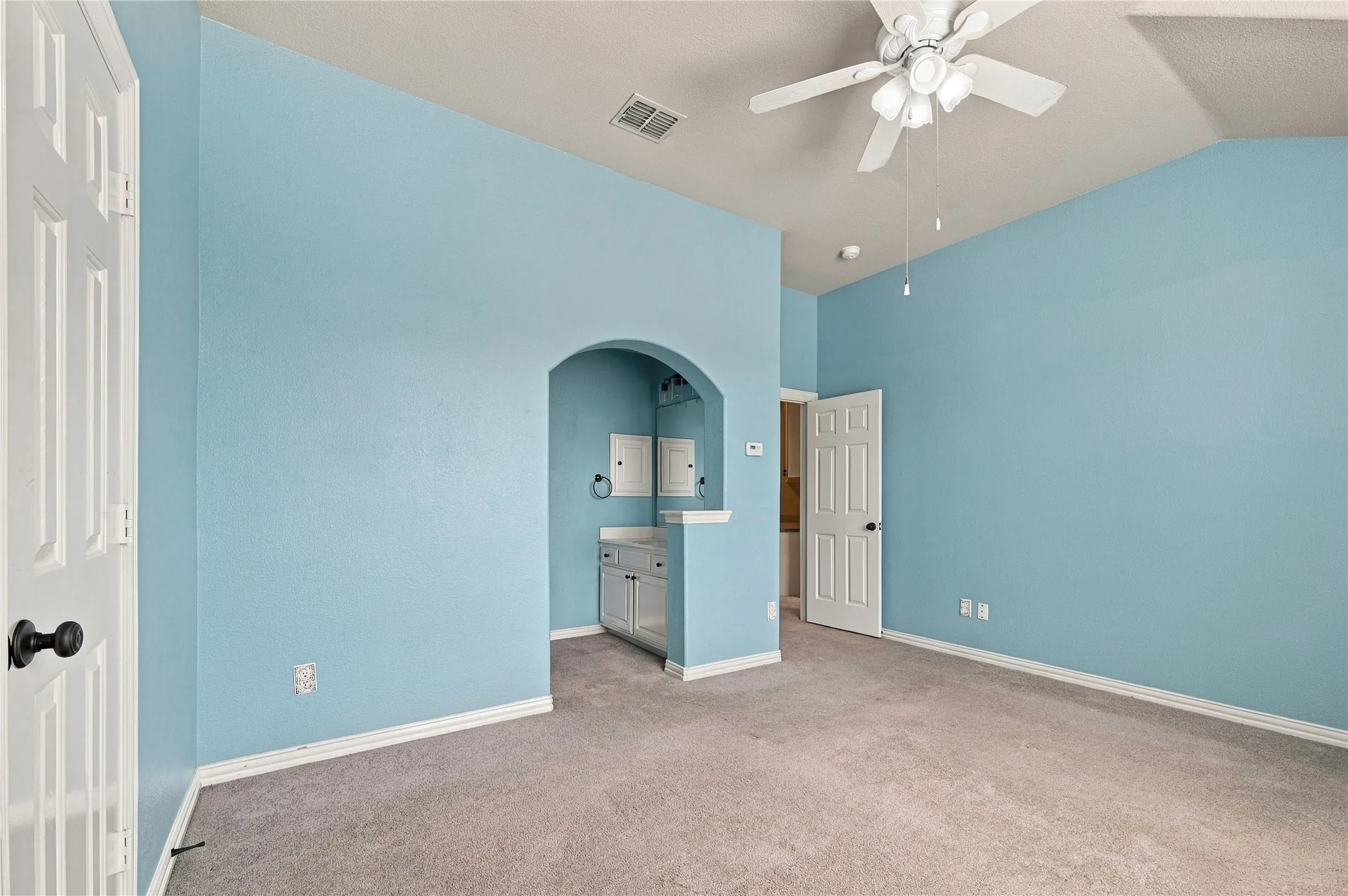 Vaulted ceiling with a ceiling fan, arched alcove, built-in cabinetry, and gray carpeting