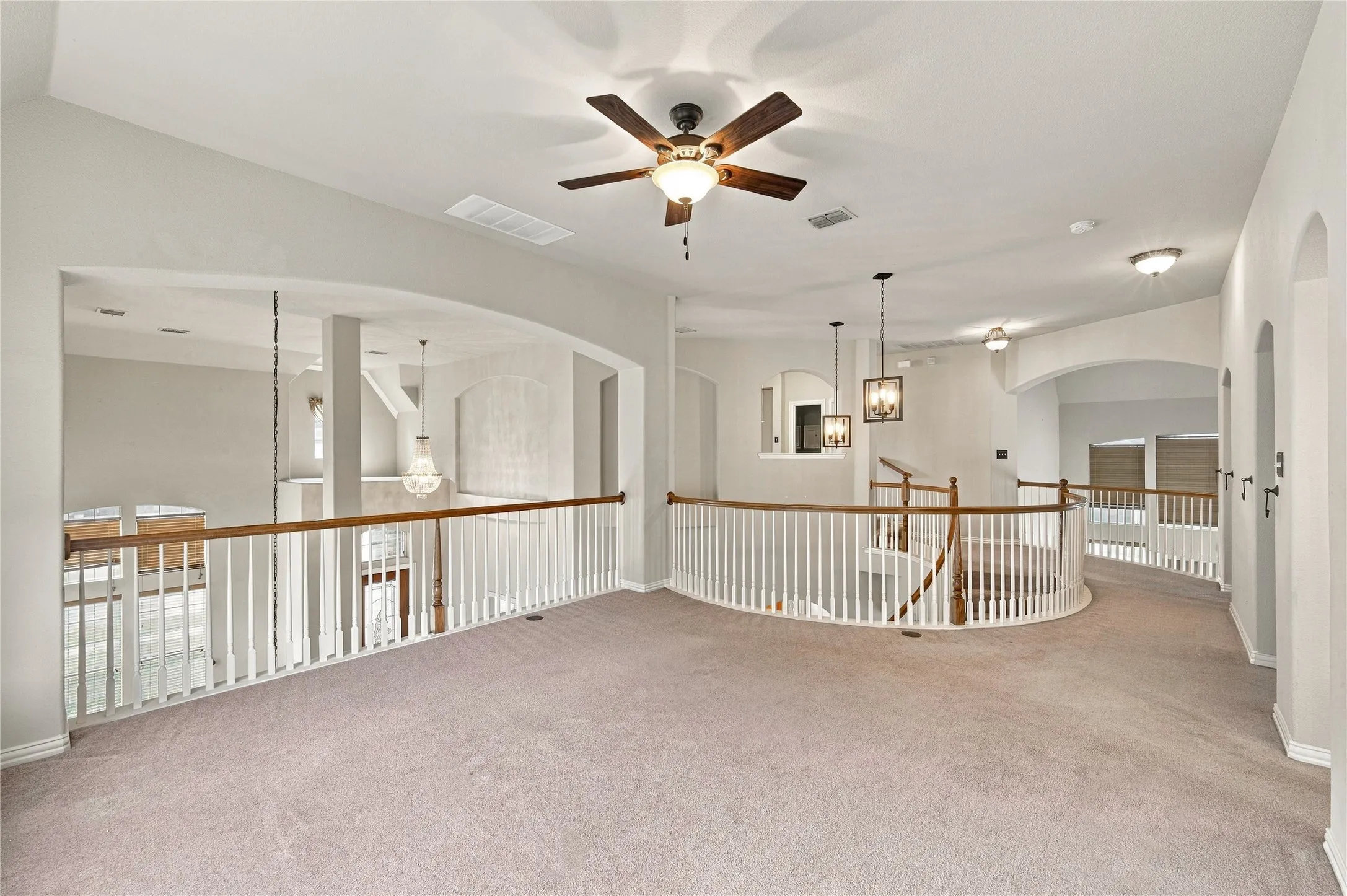 Arched doorways, ceiling fan, carpeted flooring, white baluster railings, and wood handrails