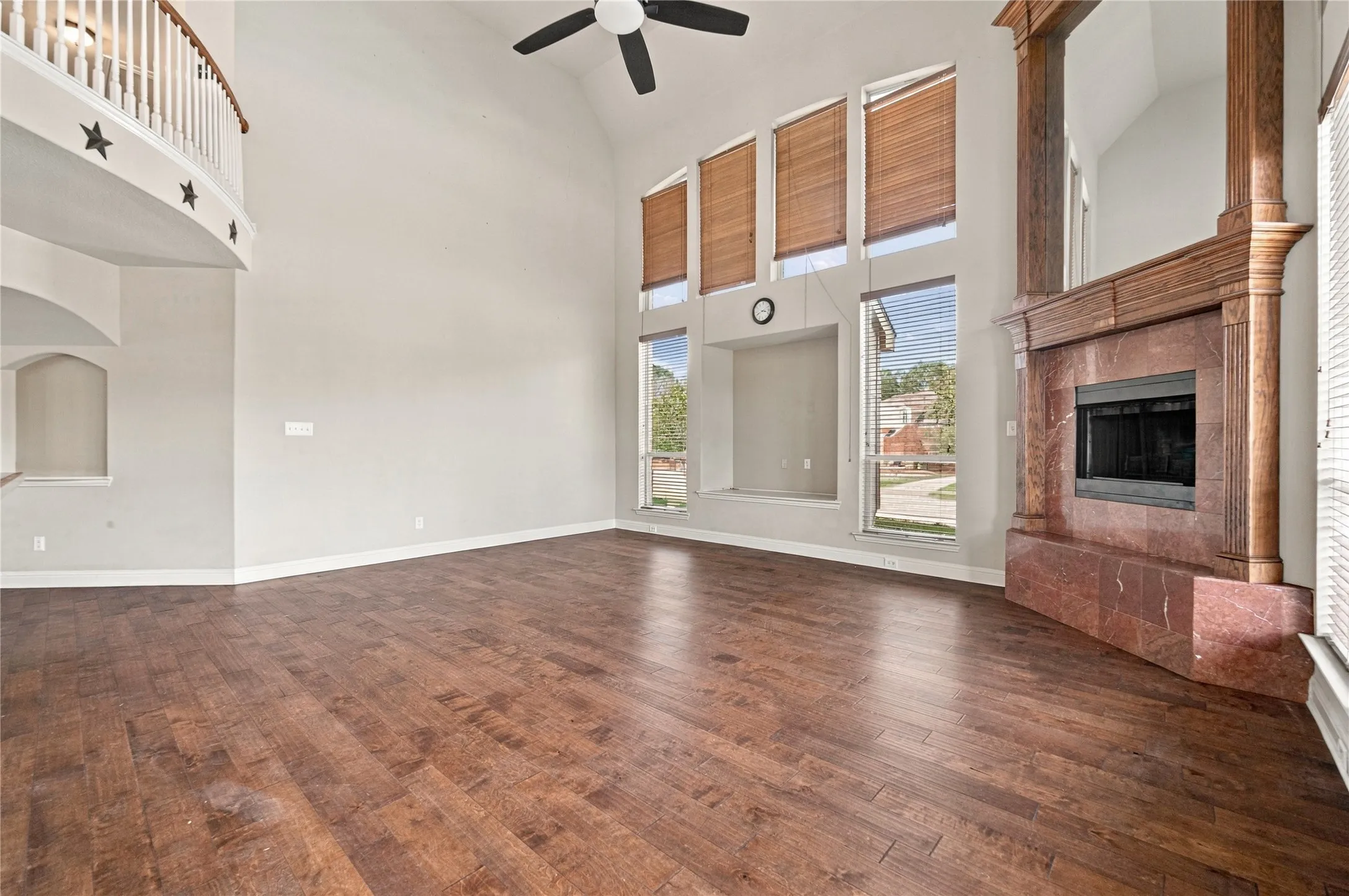 Spacious great room featuring soaring ceilings with ceiling fan, gleaming wood-finish flooring, and abundant natural light from expansive windows and glass doors