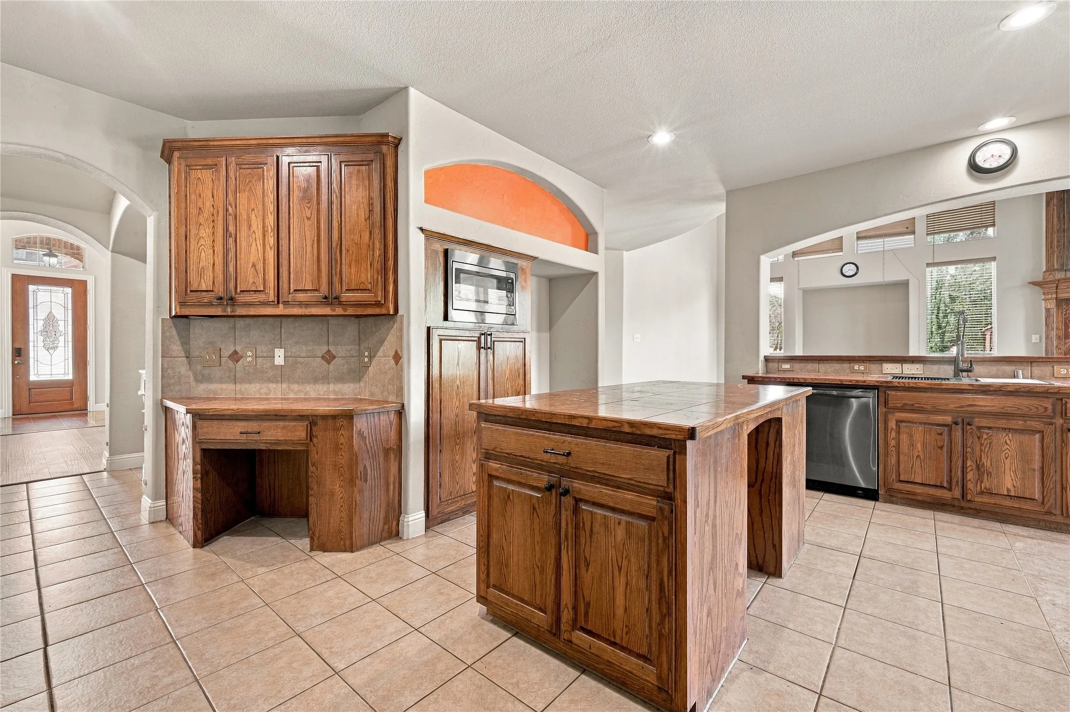 Tile flooring, wood cabinetry, built-in desk, kitchen island, and stainless steel dishwasher