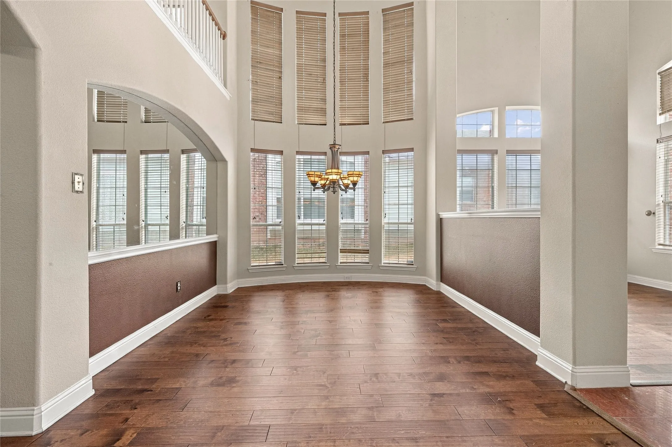 Two-story ceiling, arched entryway, upper-level railing, wood-finish flooring, and a multi-tiered chandelier