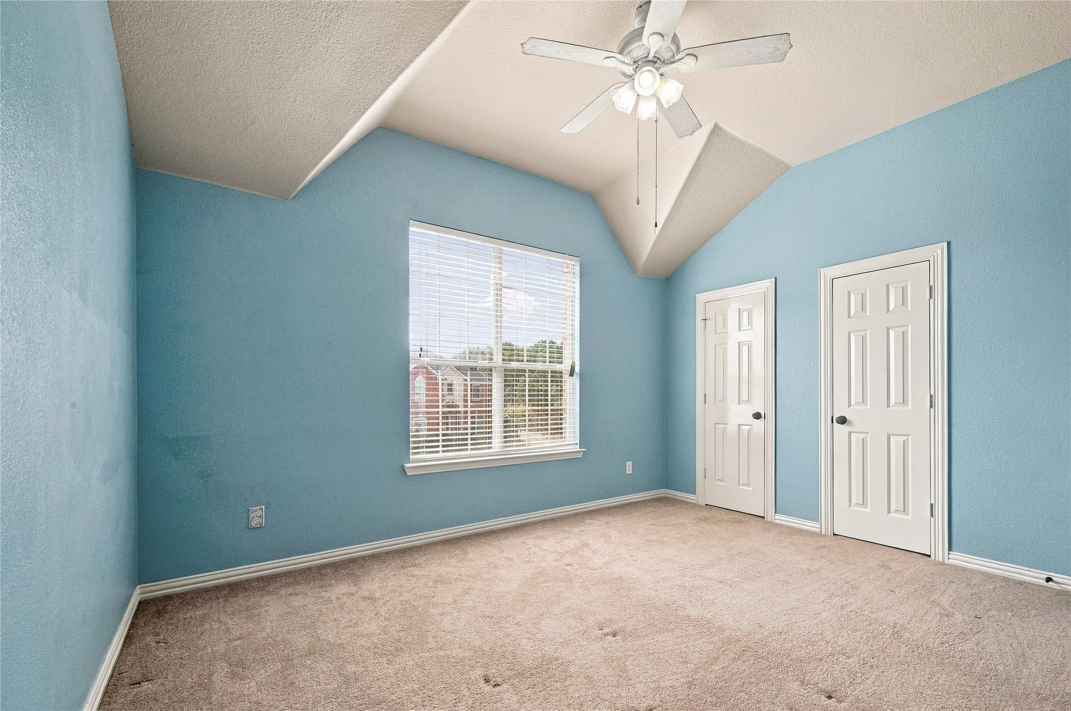 Vaulted ceiling with a ceiling fan light fixture, window with blinds, and two paneled doors