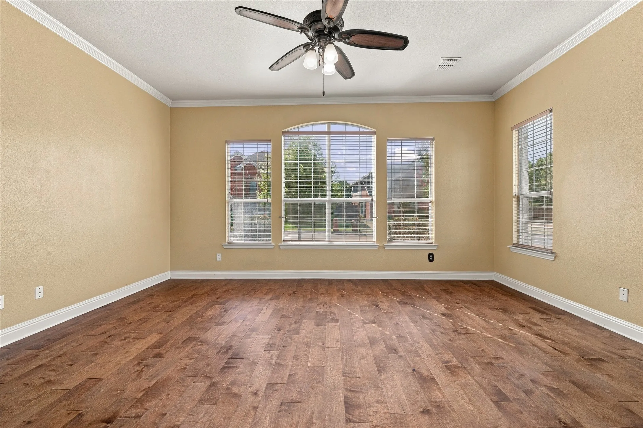 Wood-finish flooring, crown molding, and multiple windows with blinds