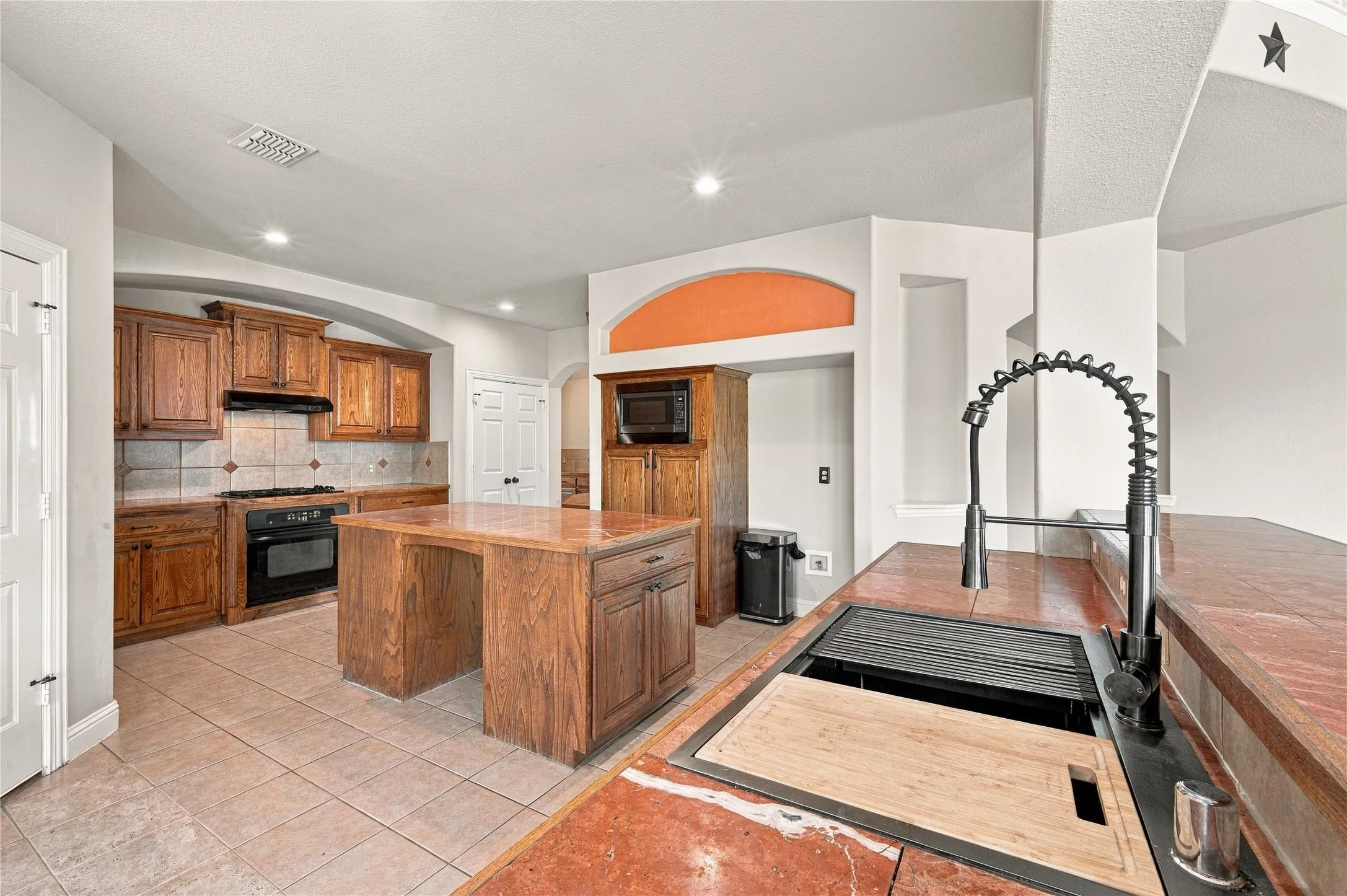 Kitchen featuring wood cabinetry, a center island, tile flooring, a tile backsplash, and a black built-in oven